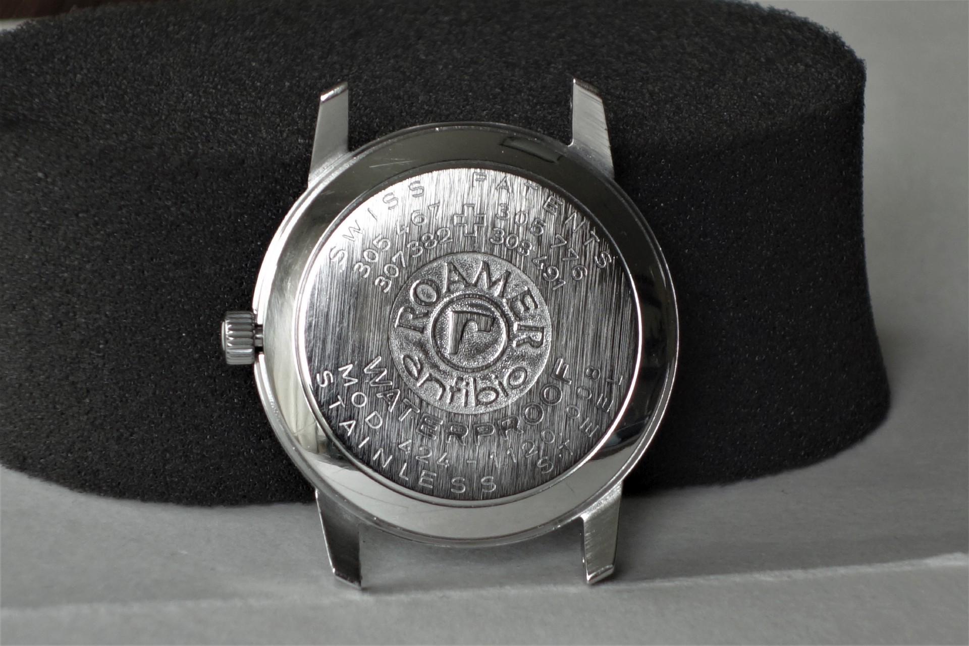 Silberfarbener Gehäuseboden einer Uhr mit eingraviertem Logo und Schriftzug.