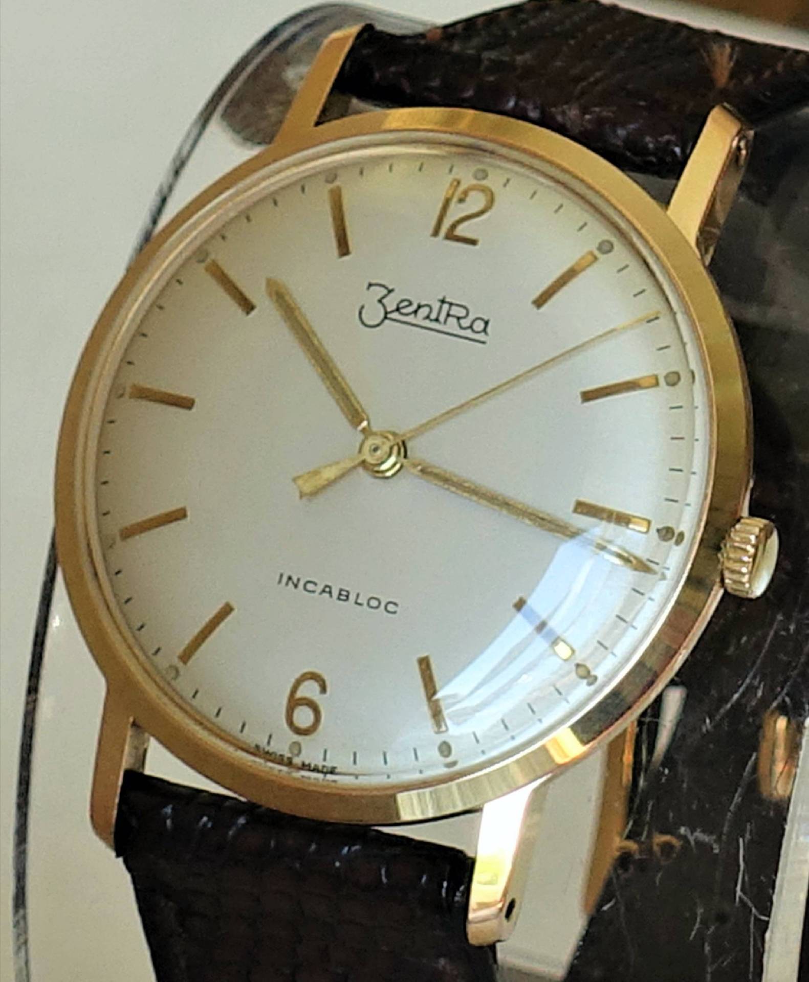 Goldfarbene Armbanduhr mit hellem Zifferblatt und braunem Armband.