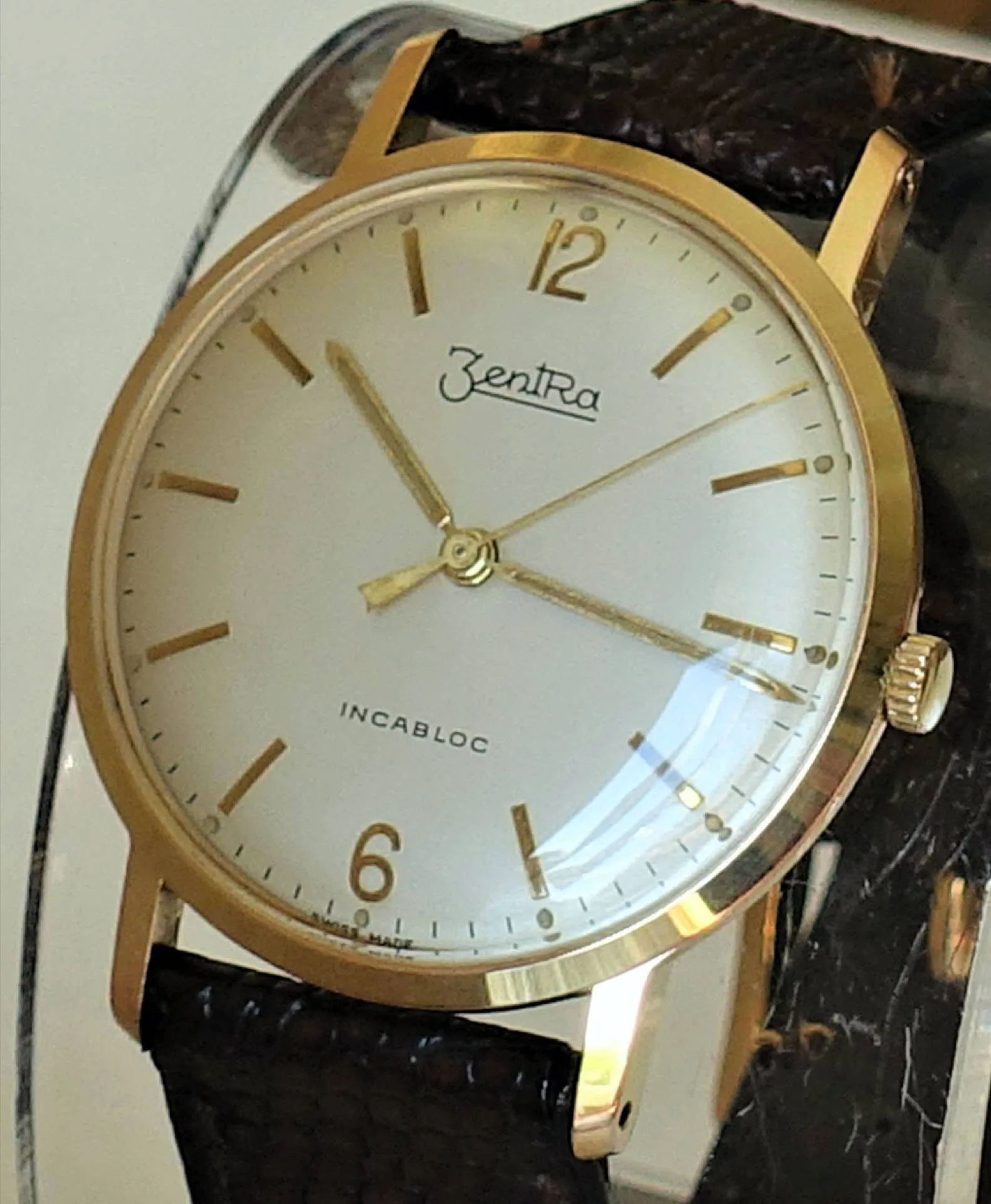 Goldfarbene Armbanduhr mit hellem Zifferblatt und braunem Armband.