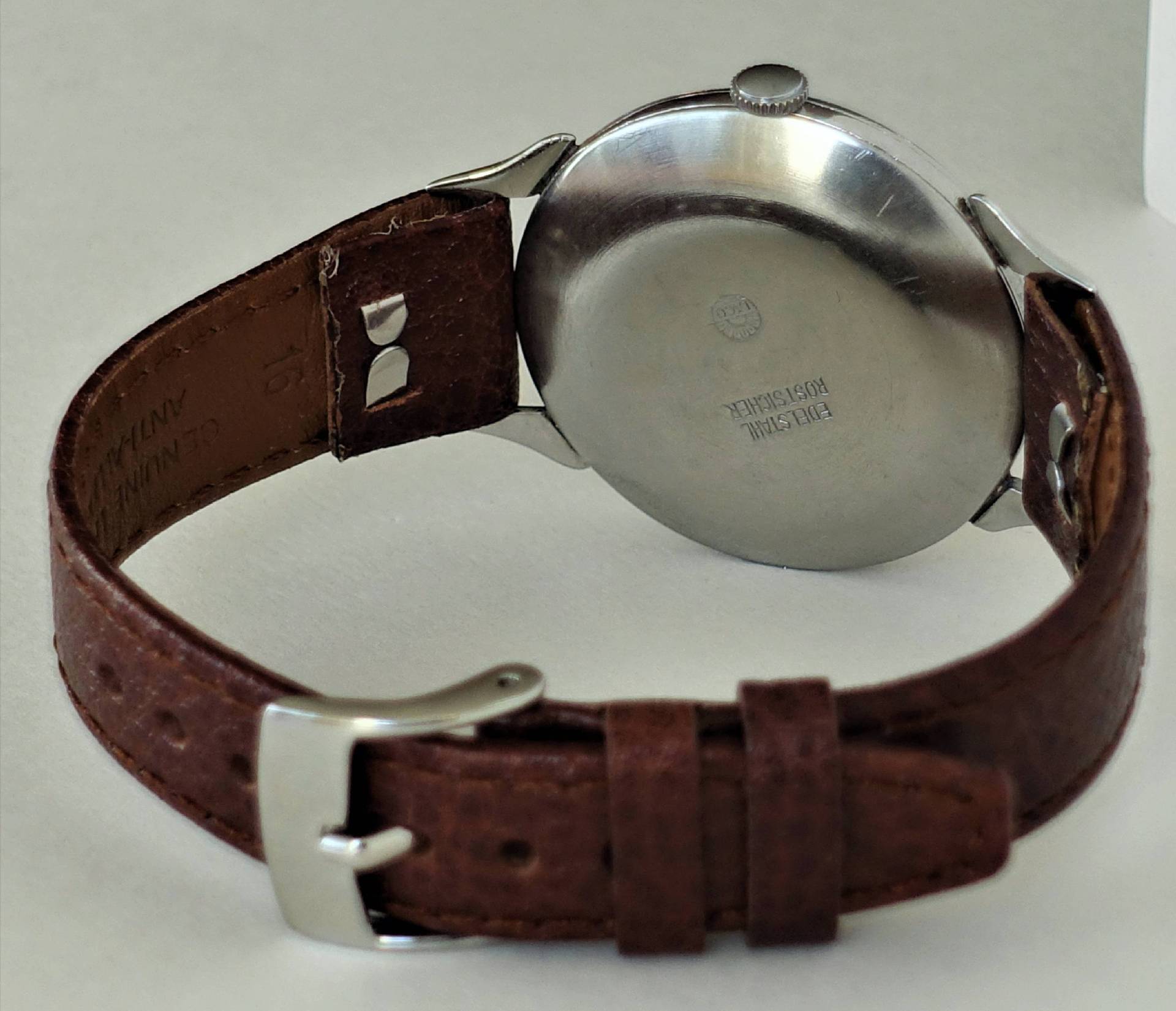 Armbanduhr mit braunem Lederarmband und silberfarbener Rückseite.