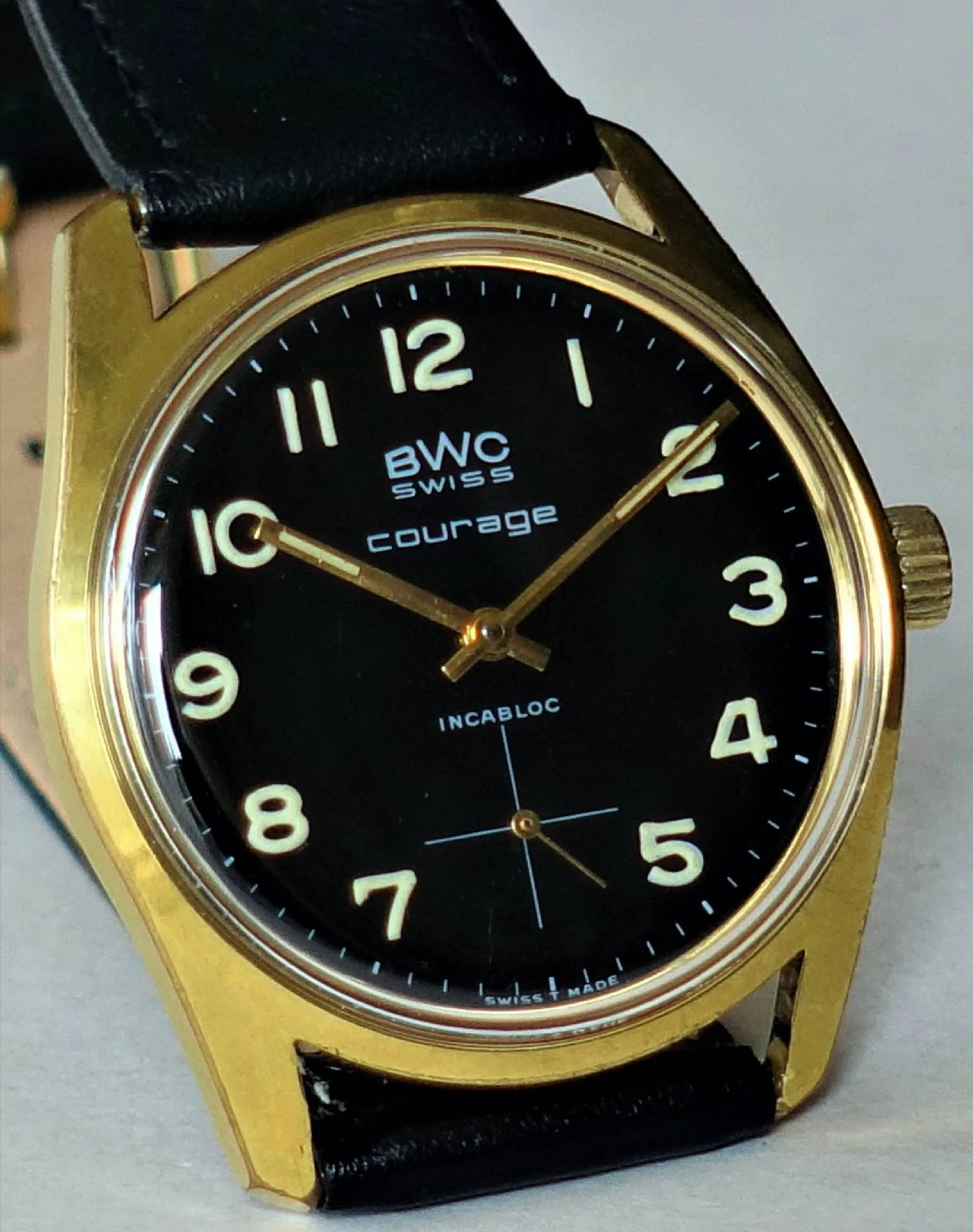 Schwarze Armbanduhr mit goldfarbenem Gehäuse und schwarzem Lederarmband.