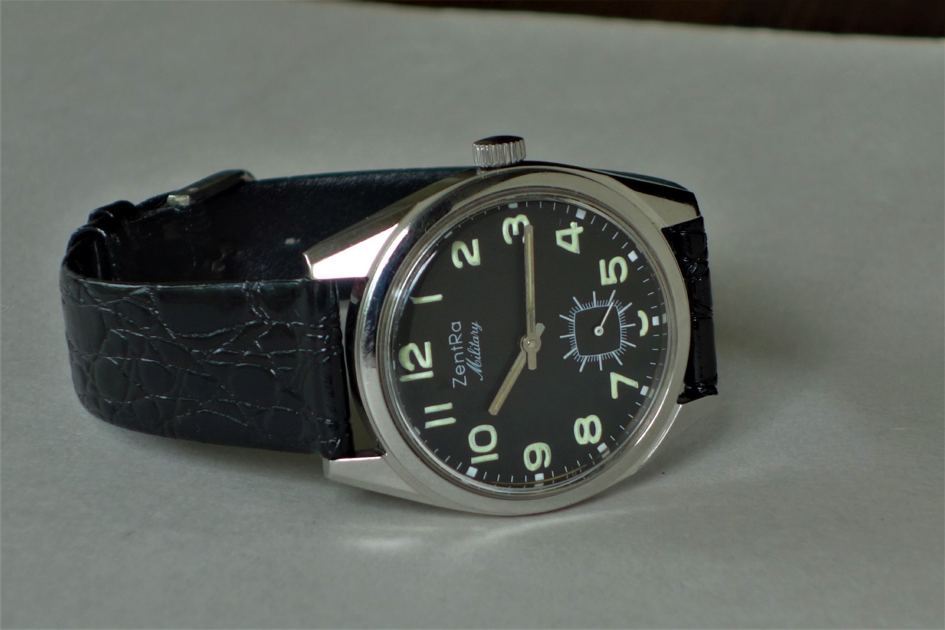 Schwarze Armbanduhr mit silberfarbenem Gehäuse und schwarzem Zifferblatt, darauf leuchtende Ziffern und ein schwarzes Armband.