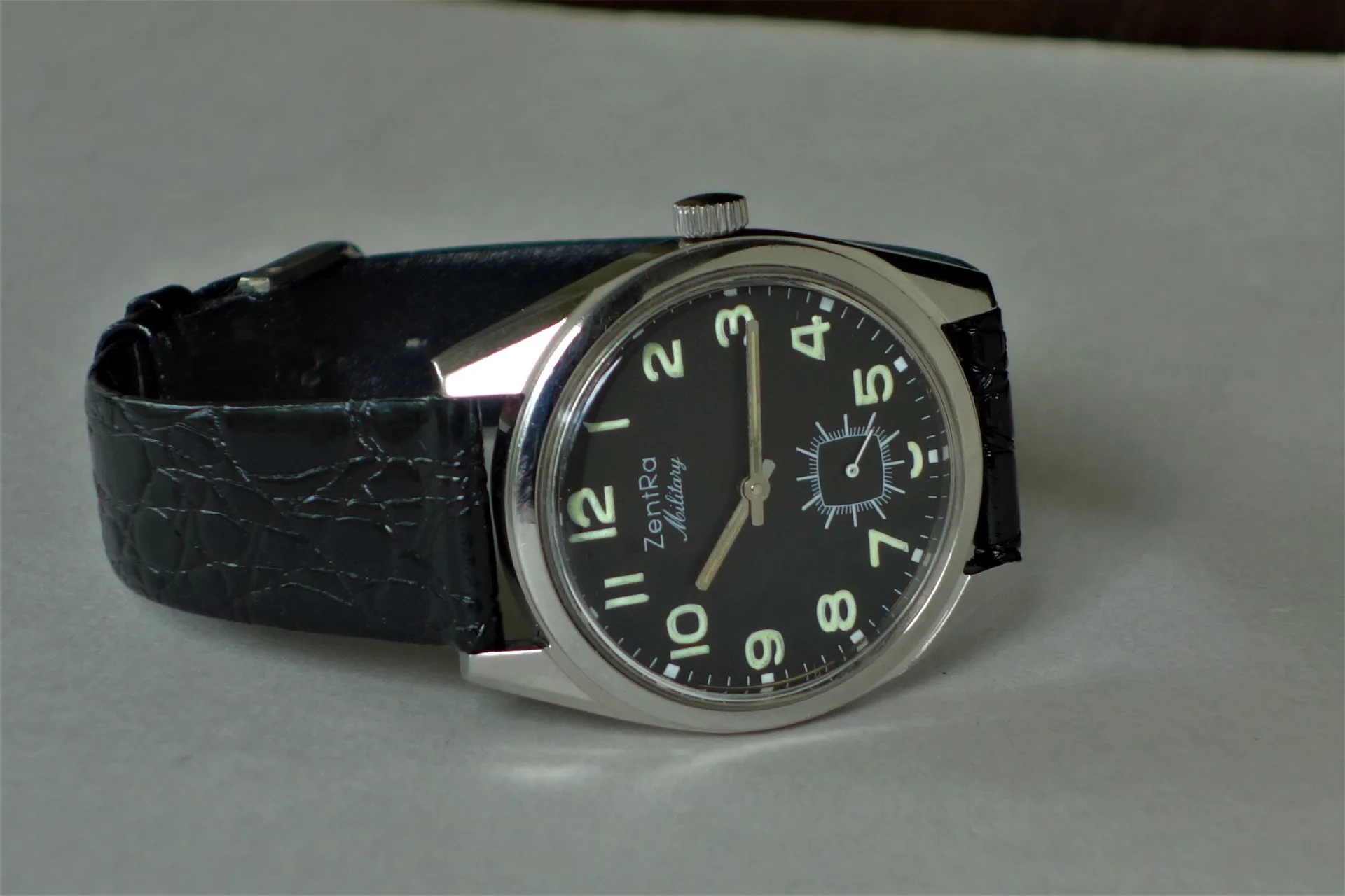 Schwarze Armbanduhr mit silberfarbenem Gehäuse und schwarzem Zifferblatt, darauf leuchtende Ziffern und ein schwarzes Armband.