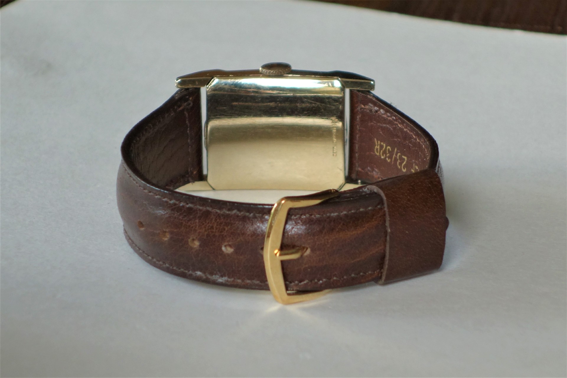 Rechteckige Armbanduhr mit braunem Lederarmband und goldfarbenem Gehäuse.