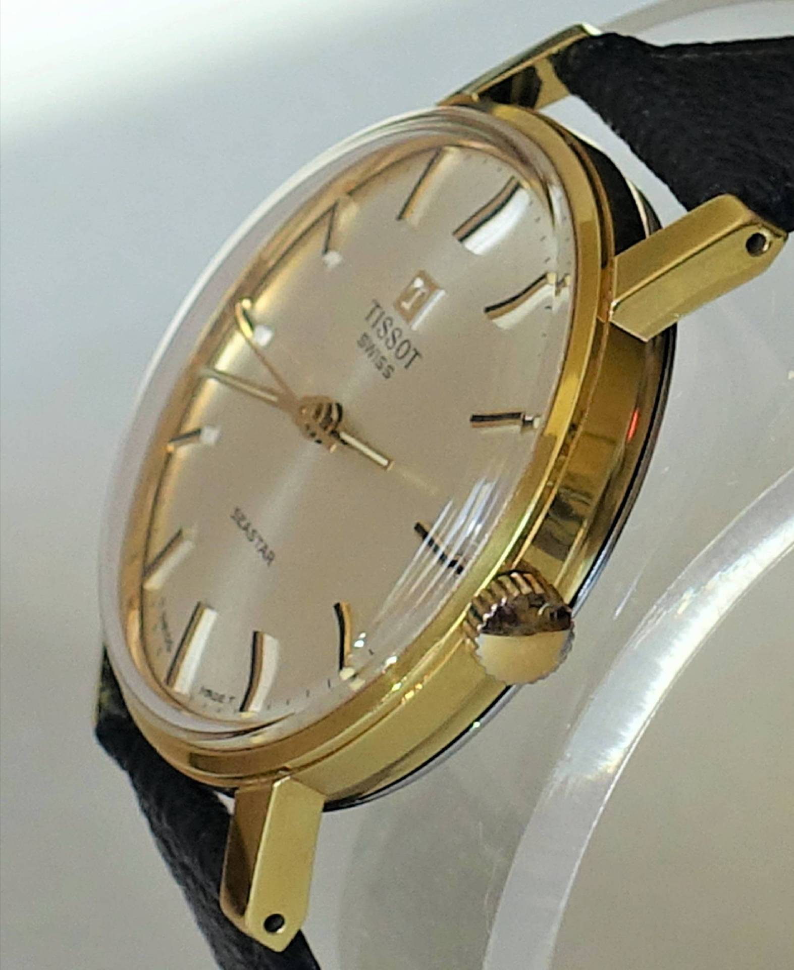 Goldfarbene Armbanduhr mit hellem Zifferblatt und schwarzem Armband.
