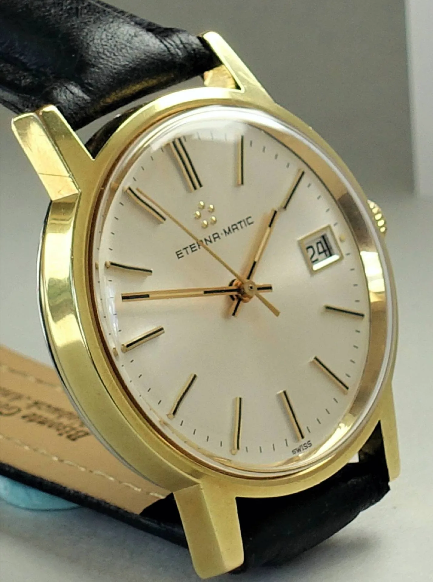 Goldfarbene Armbanduhr mit hellem Zifferblatt, schwarzen Indizes und schwarzem Lederarmband.