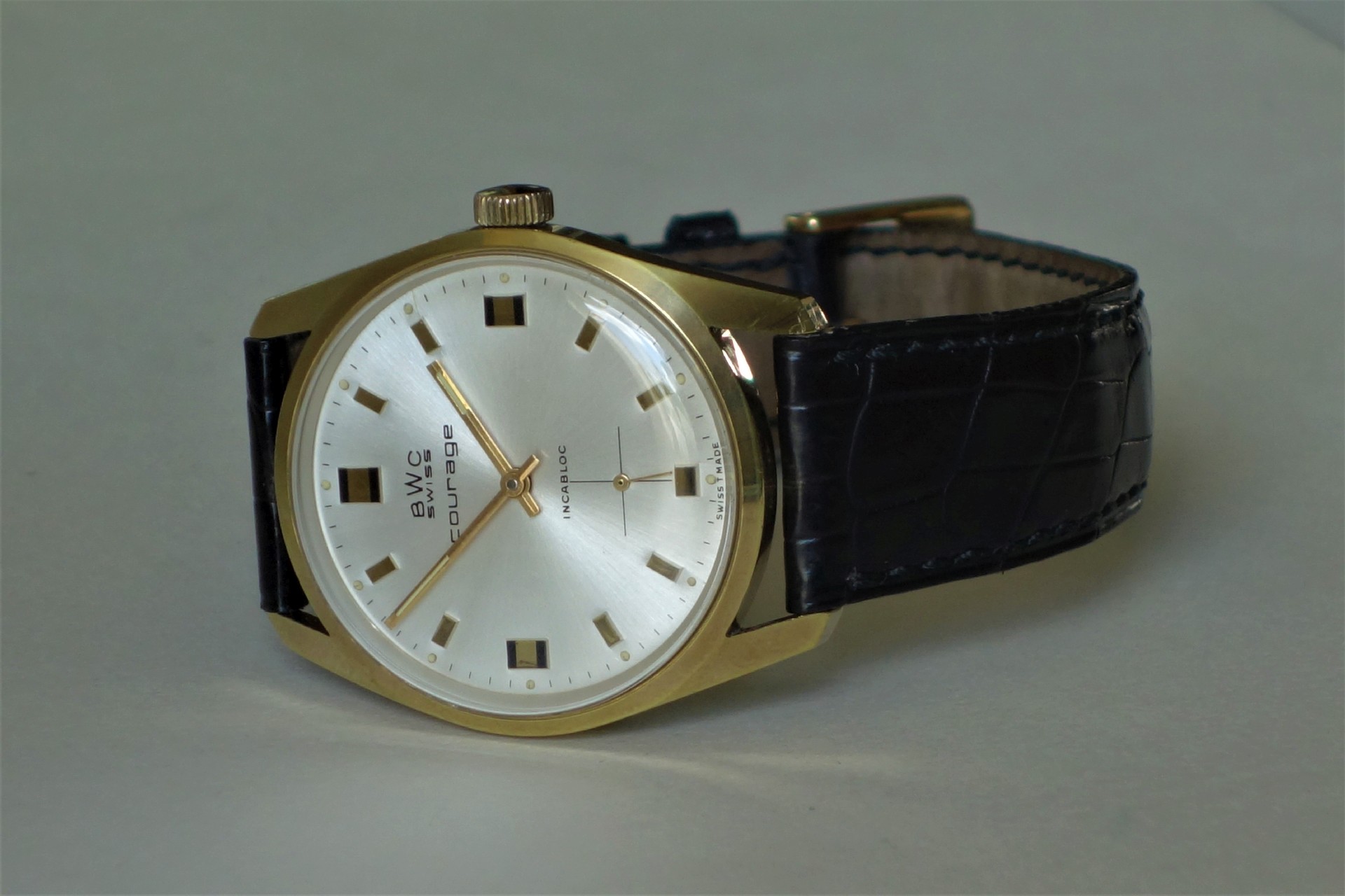 Goldfarbene Armbanduhr mit hellem Zifferblatt und schwarzem Lederarmband.