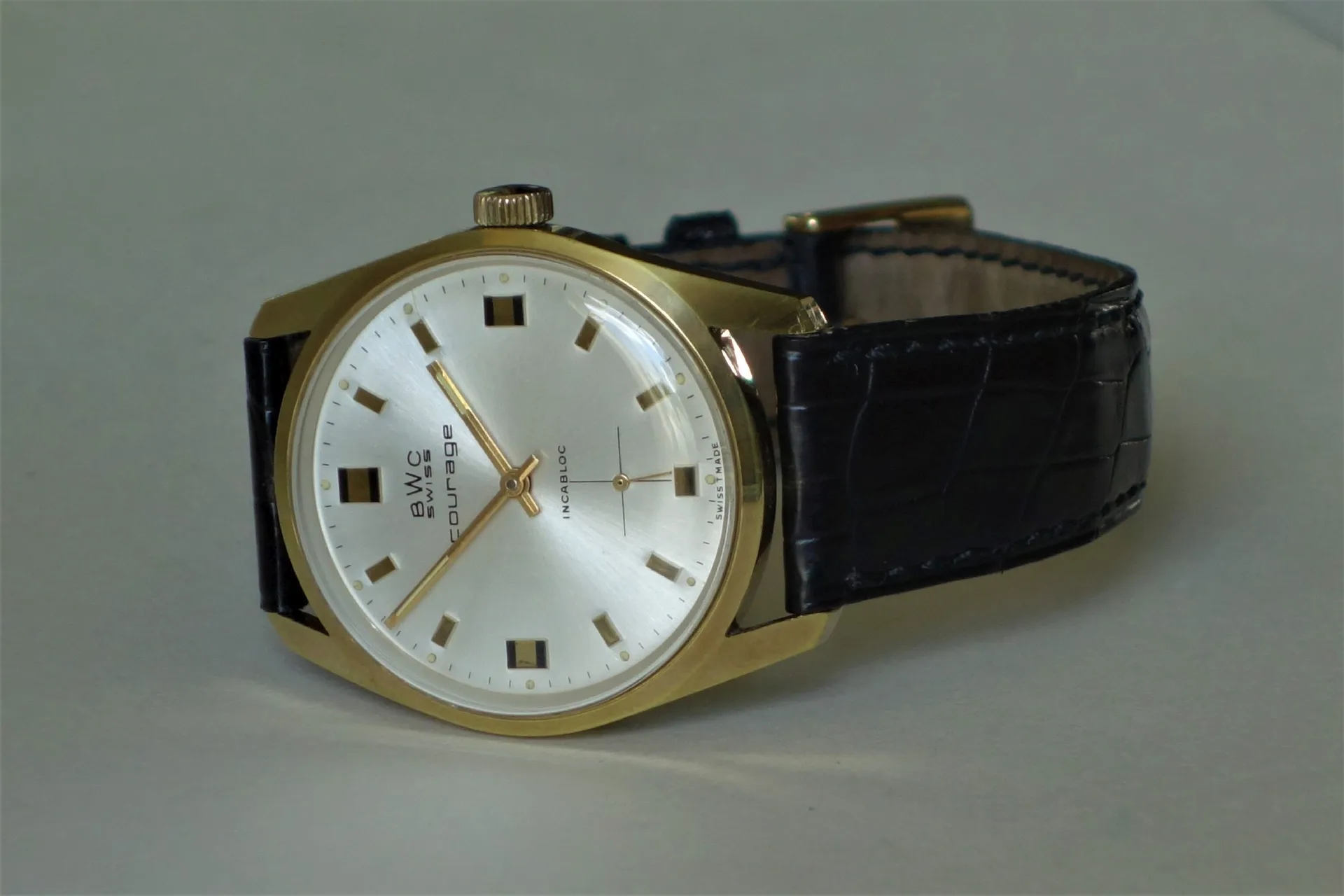 Goldfarbene Armbanduhr mit hellem Zifferblatt und schwarzem Lederarmband.
