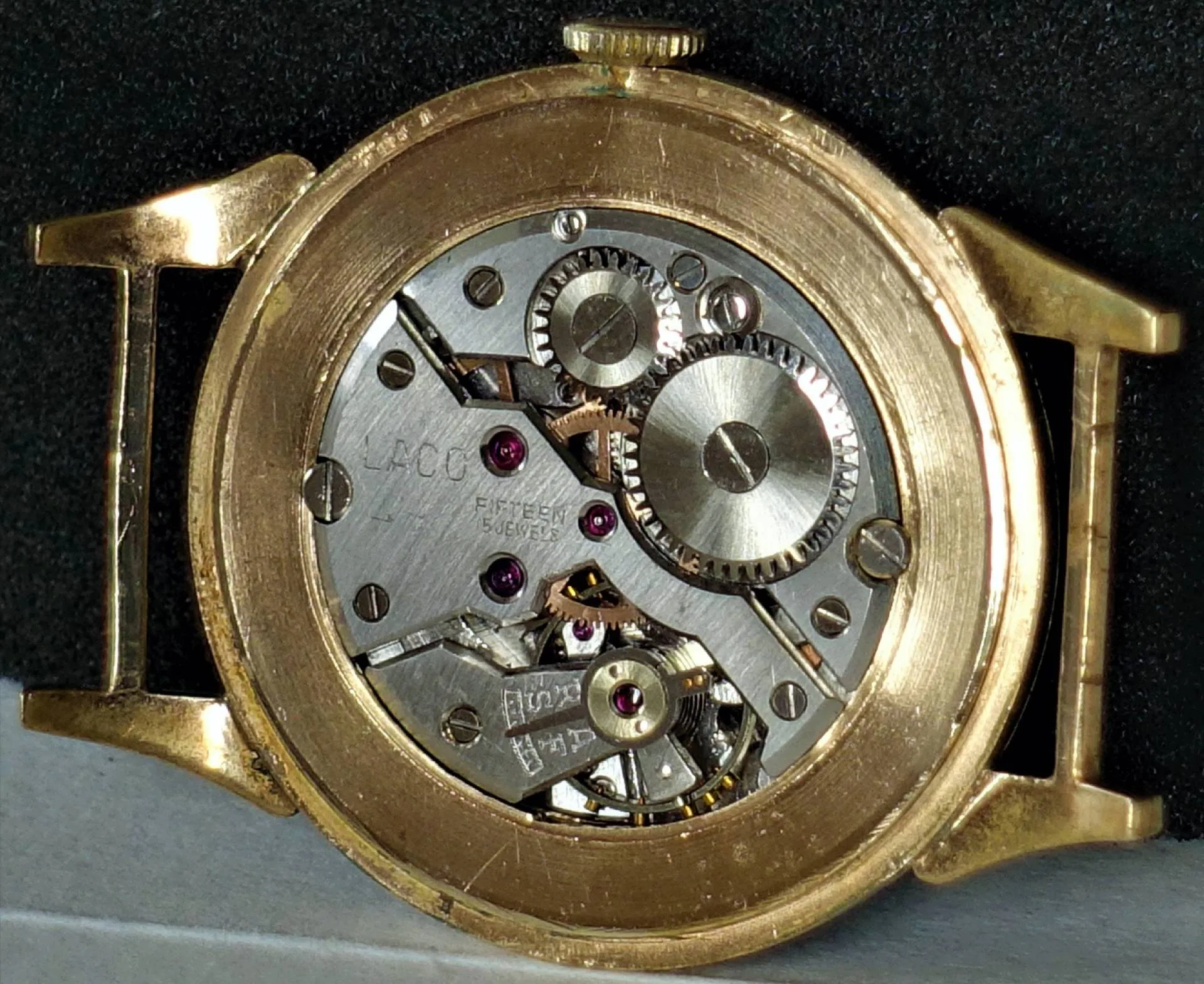 Rückseite einer Armbanduhr mit goldfarbenem Gehäuse und sichtbarem silberfarbenem mechanischem Uhrwerk mit Zahnrädern und roten Lagersteinen.
