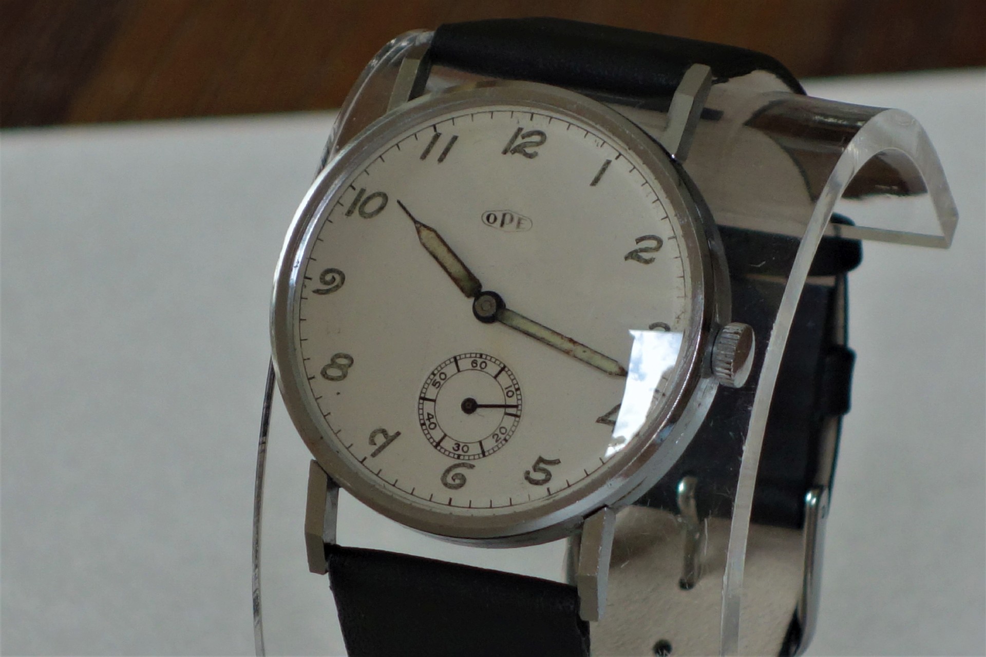 Silberfarbene Armbanduhr mit weißem Zifferblatt und schwarzem Lederarmband.