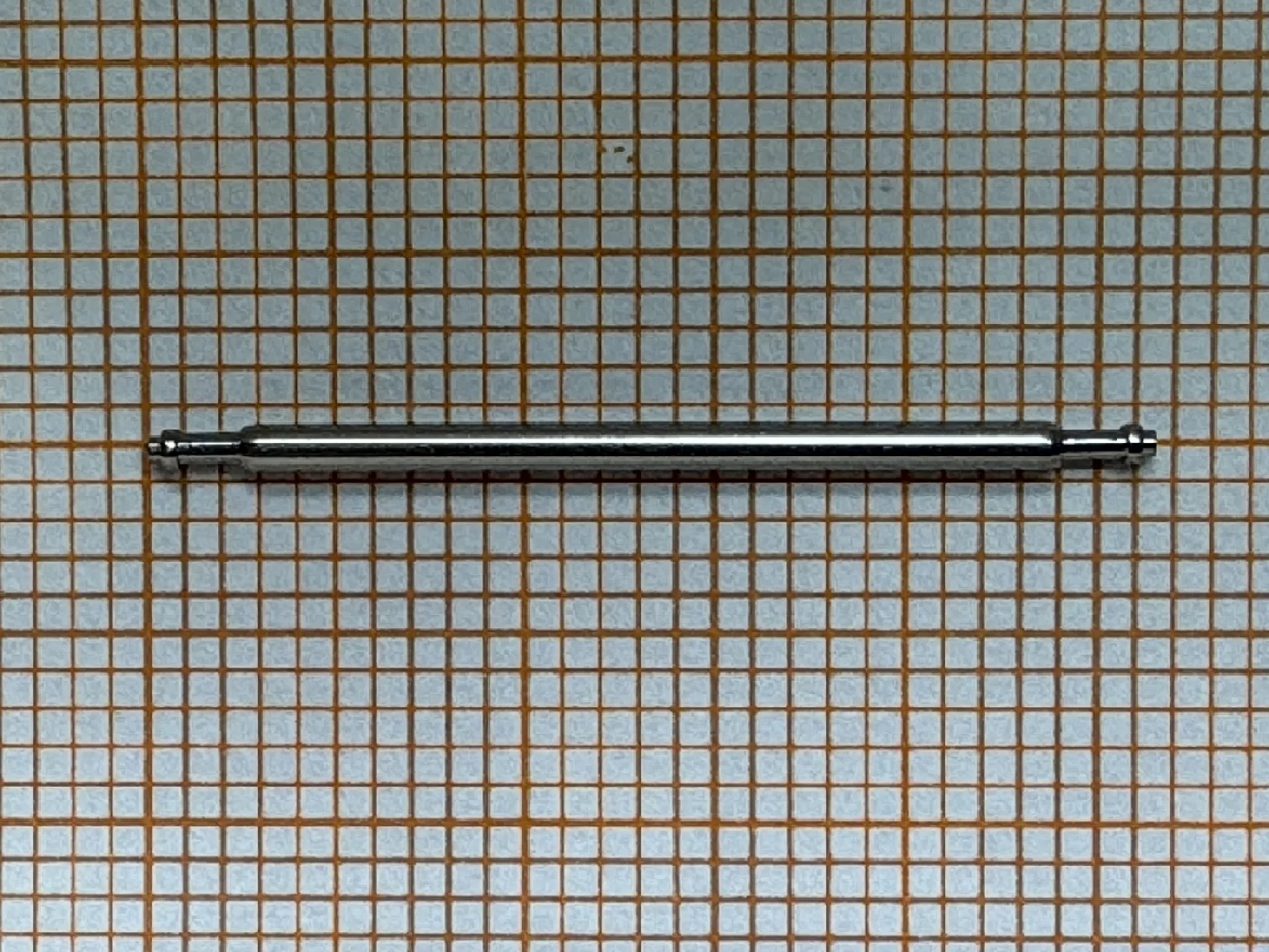 Metallischer Federsteg für Uhrenarmbänder auf kariertem Hintergrund.