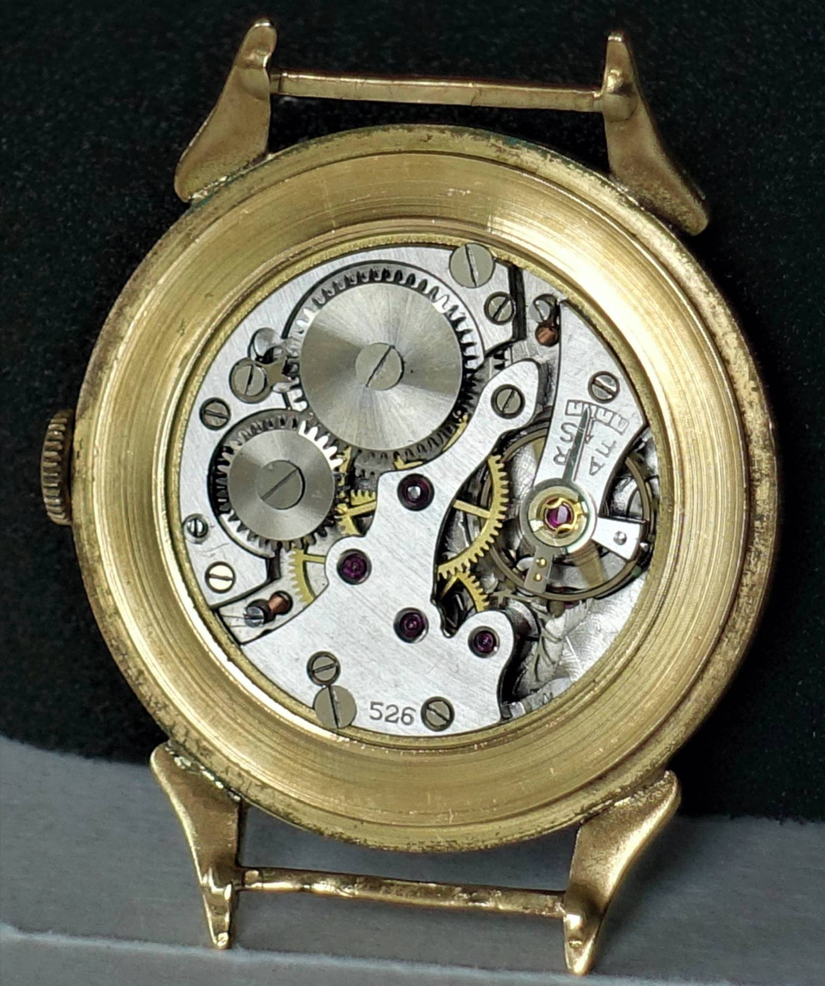 Mechanisches Uhrwerk in einem goldfarbenen Uhrengehäuse, sichtbare Zahnräder und Schrauben.