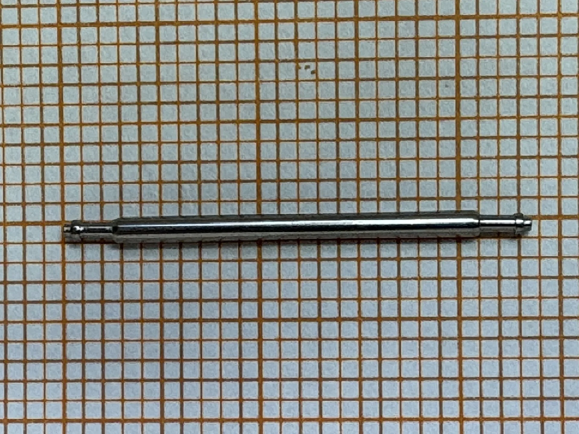 Metallischer Federsteg für Uhrenarmbänder auf kariertem Hintergrund.