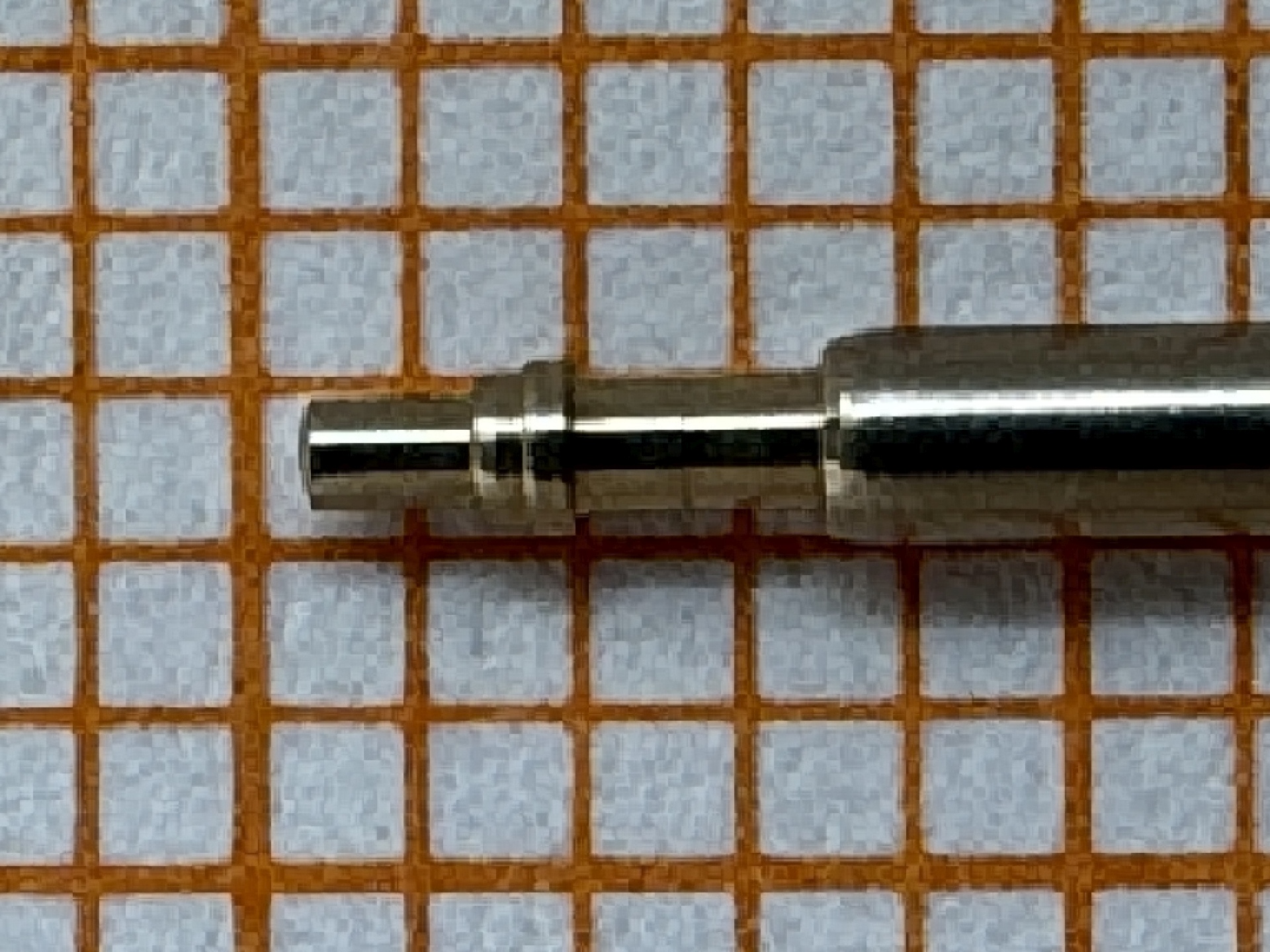 Metallene Aufzugswelle für Armbanduhren auf kariertem Hintergrund.