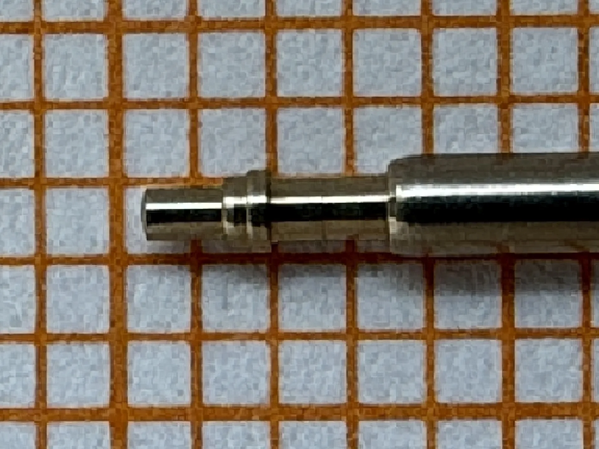 Metallene Aufzugswelle für Armbanduhren auf kariertem Hintergrund.