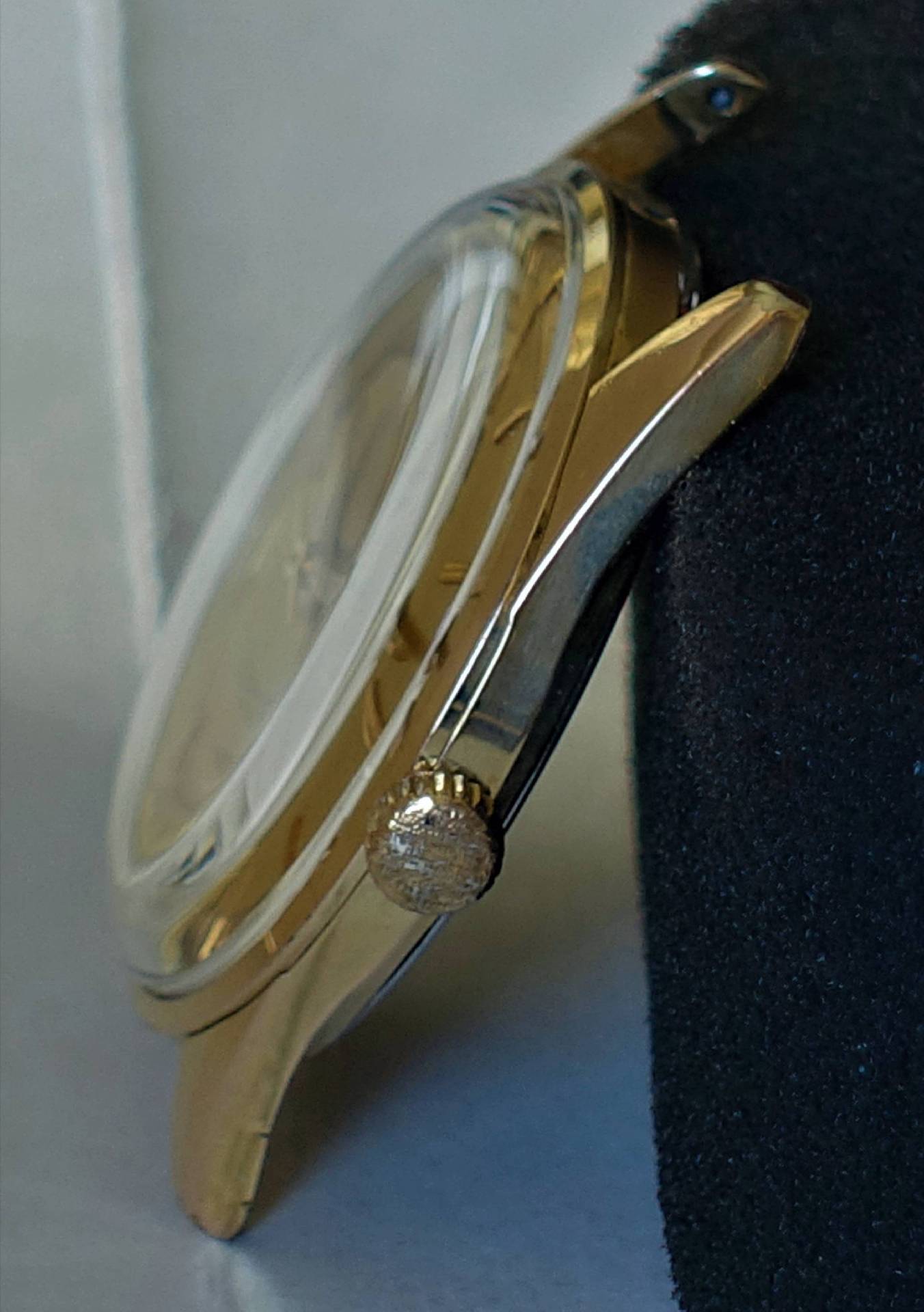 Seitliche Ansicht eines goldfarbenen Uhrgehäuses mit Krone und Glas.