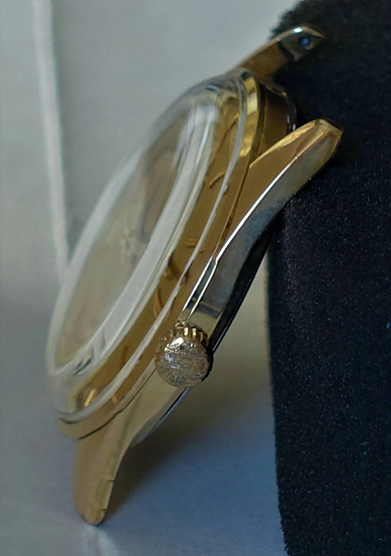Seitliche Ansicht eines goldfarbenen Uhrgehäuses mit Krone und Glas.