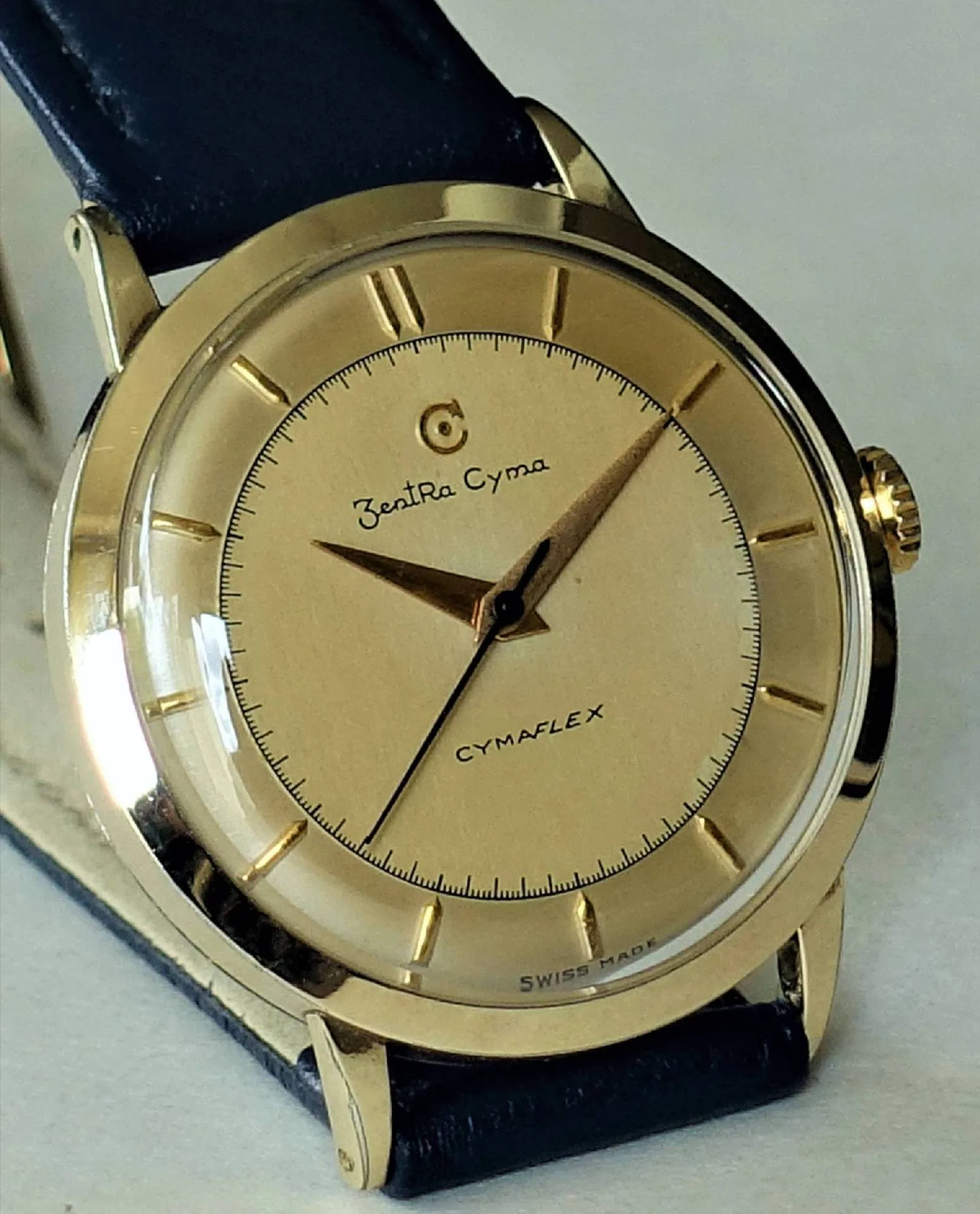 ZentRa Cyma Armbanduhr Goldfarbene Armbanduhr mit hellem Zifferblatt und schwarzem Lederarmband.