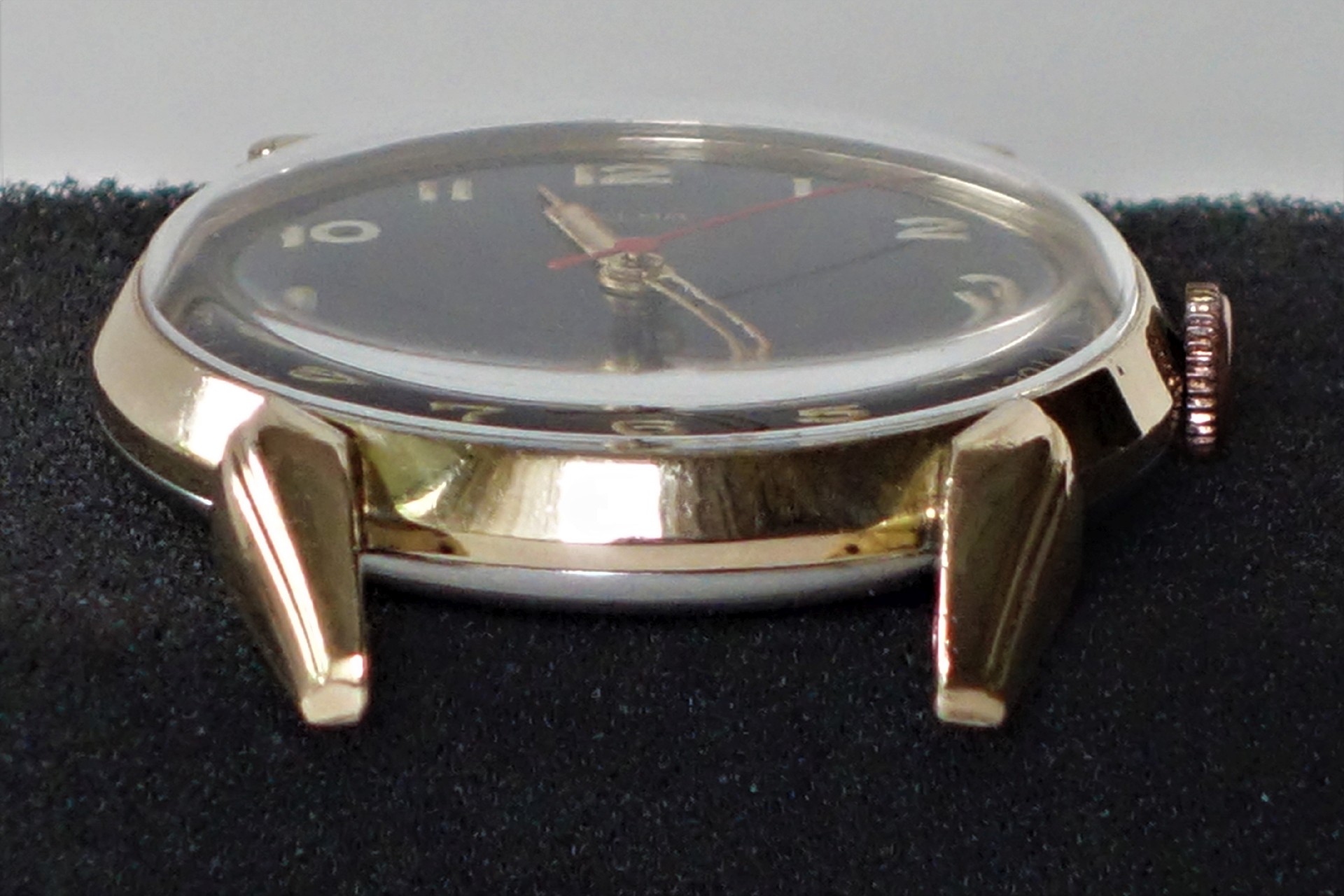 Flache analoge Armbanduhr mit goldfarbenem Gehäuse und schwarzem Zifferblatt.