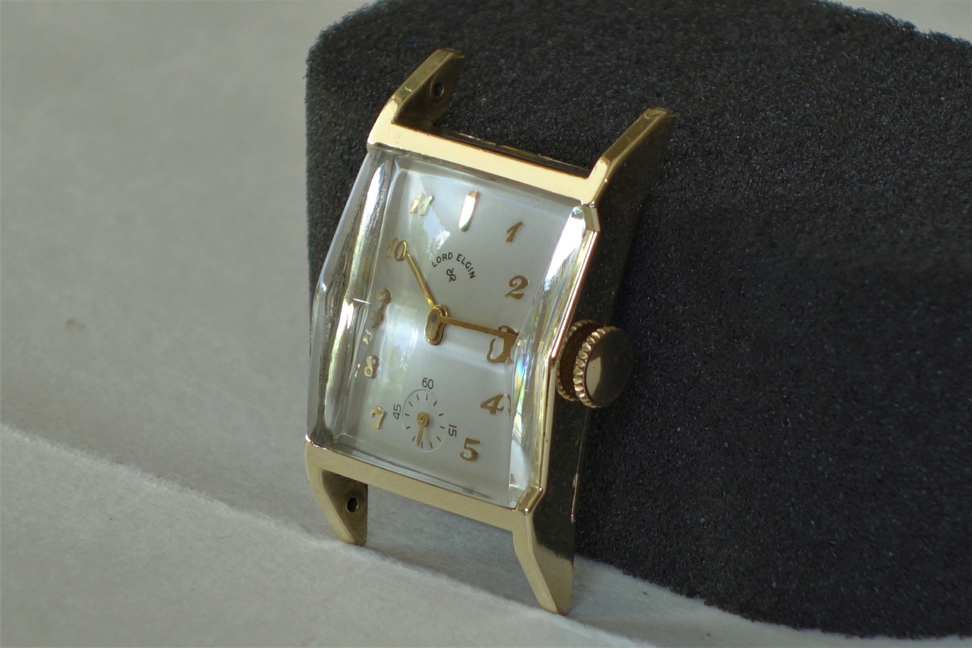Rechteckige Armbanduhr mit goldfarbenem Gehäuse und weißem Zifferblatt.