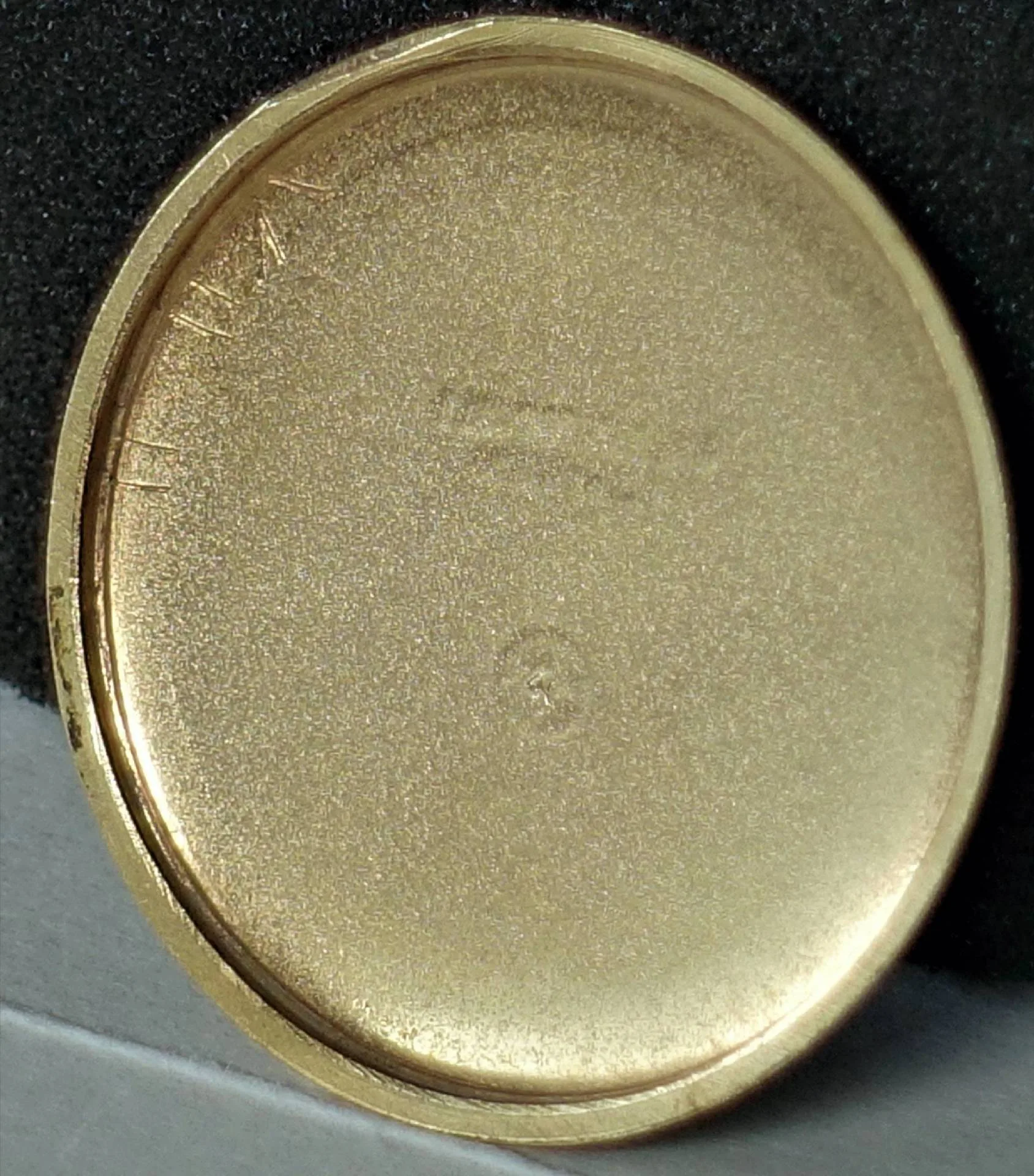Goldfarbener Uhrendeckel Innenseite Die Innenseite eines goldfarbenen Uhrendeckels ist zu sehen, mit feiner Struktur und leichter Gravur.