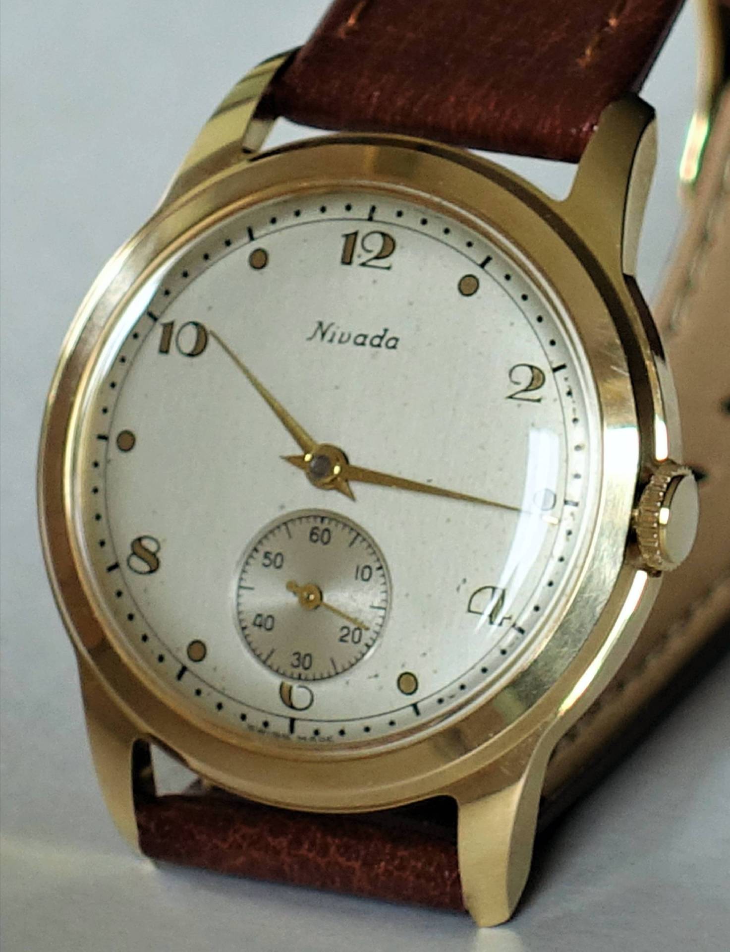 Goldfarbene Armbanduhr mit weißem Zifferblatt und braunem Lederarmband.