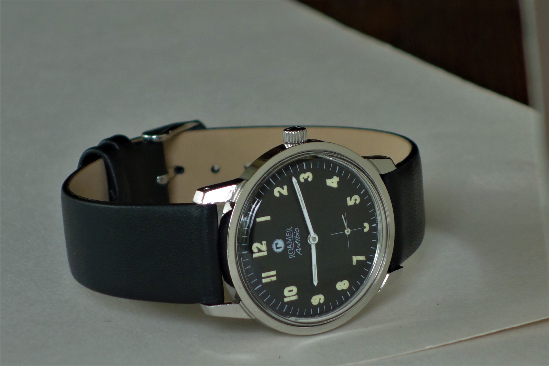 Schwarze Armbanduhr mit hellem Zifferblatt und Lederarmband.