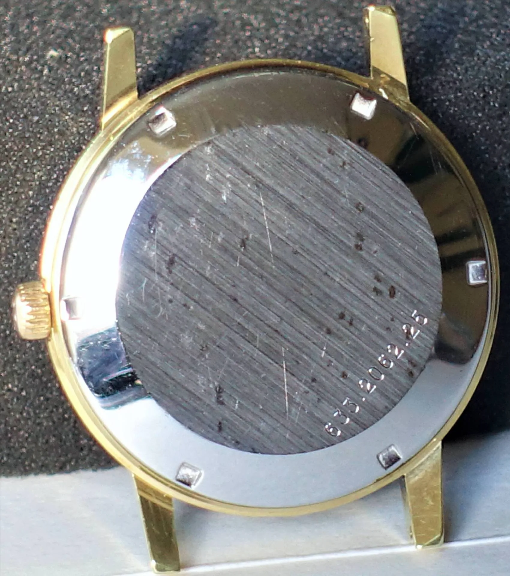 Rückseite eines goldfarbenen Uhrgehäuses mit silberfarbener Bodenplatte.
