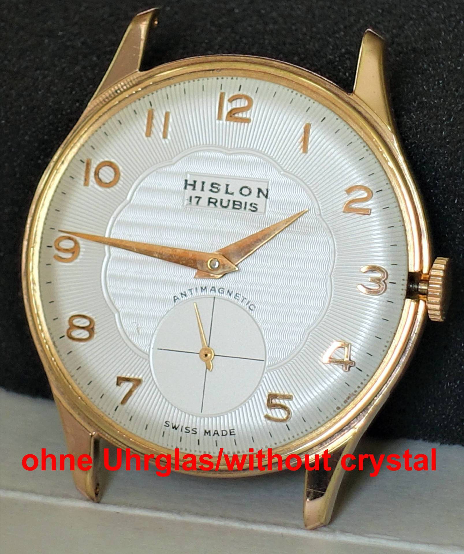 Eine goldfarbene Armbanduhr mit weißem Zifferblatt und goldfarbenen Zahlen und Zeigern, bei der das Uhrglas fehlt.