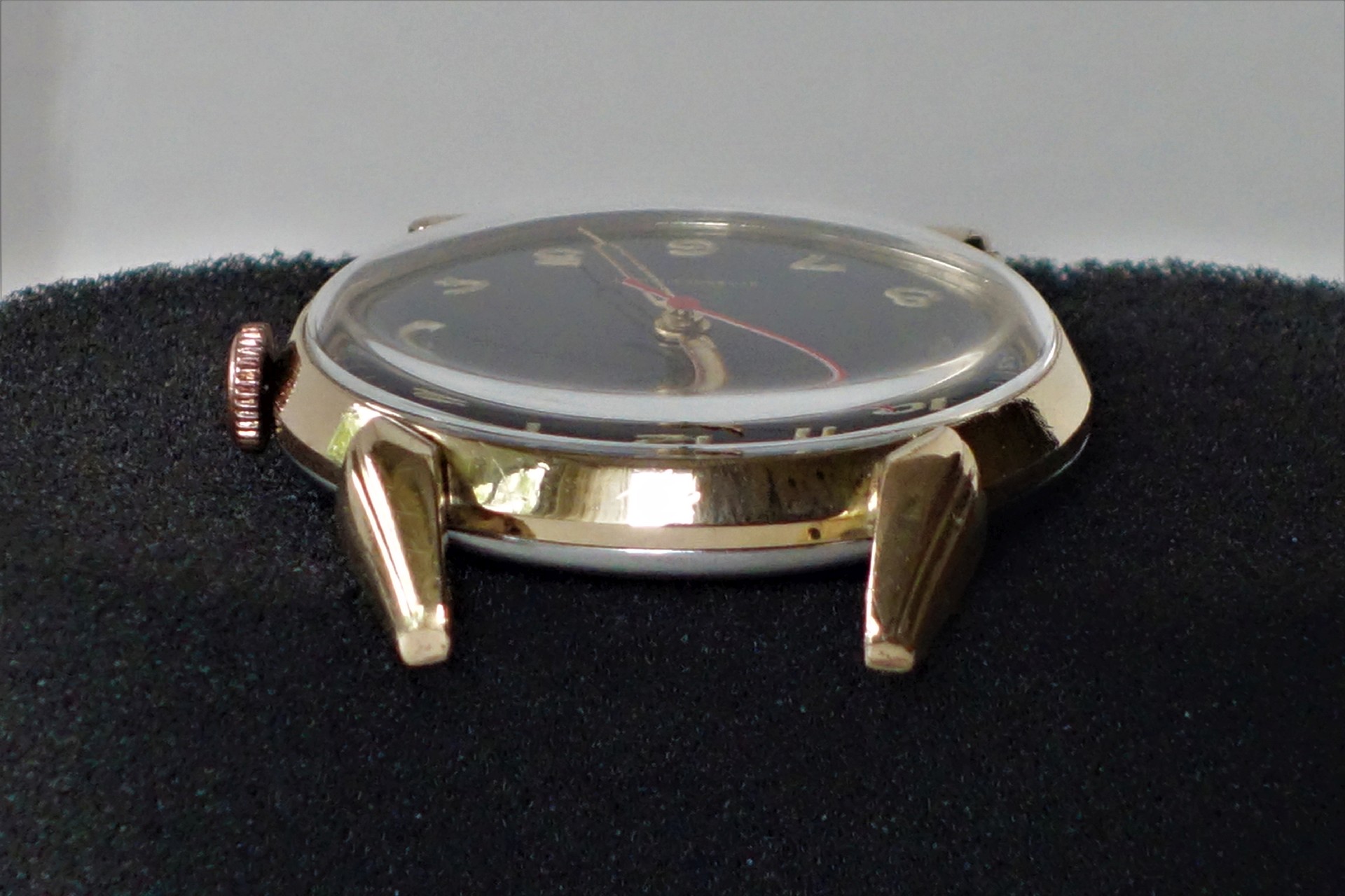 Goldfarbenes Uhrgehäuse mit schwarzem Zifferblatt und Glasabdeckung.