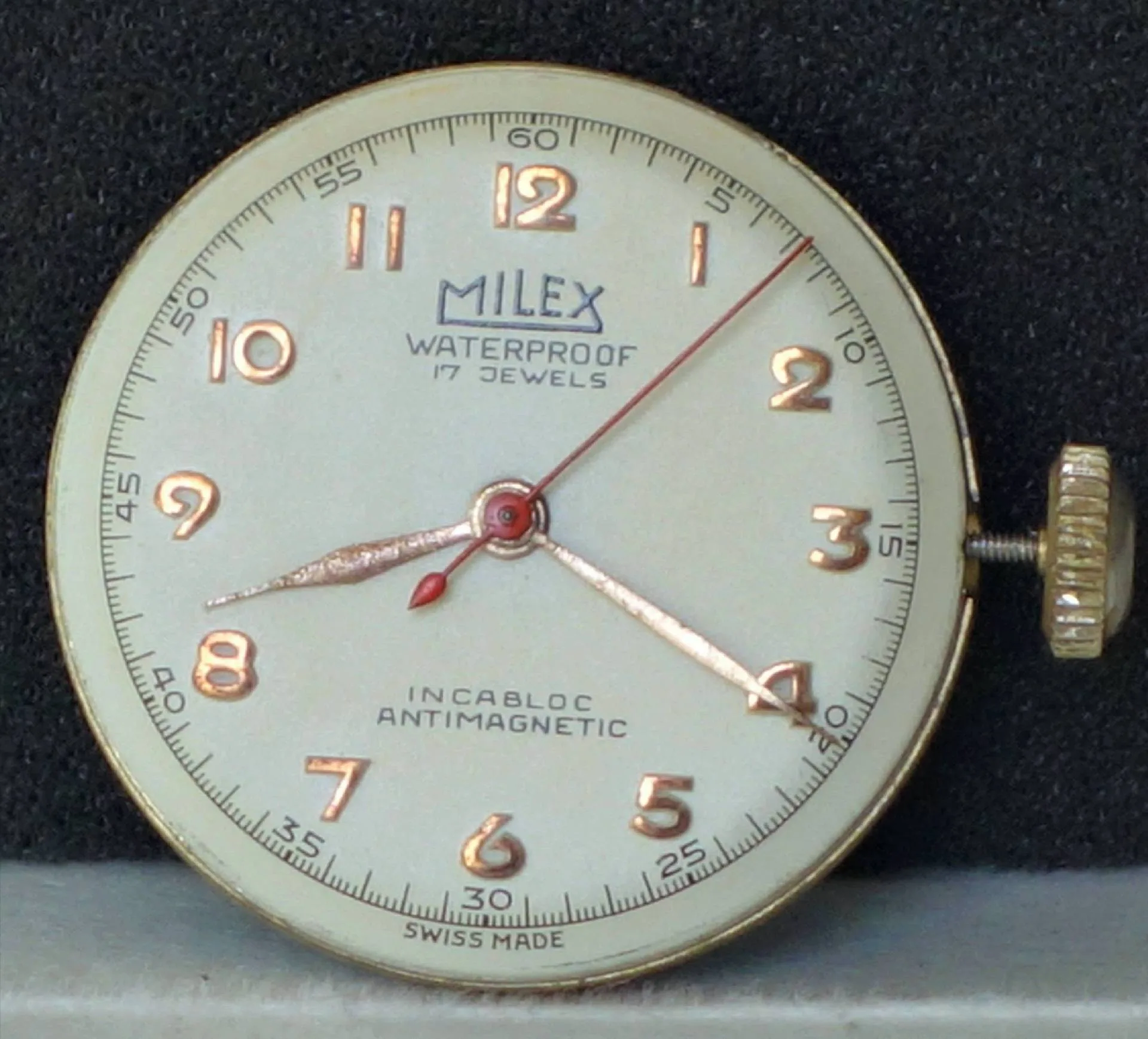Rundes mechanisches Uhrwerk mit weißem Zifferblatt und goldfarbenen Zahlen sowie Zeigern.