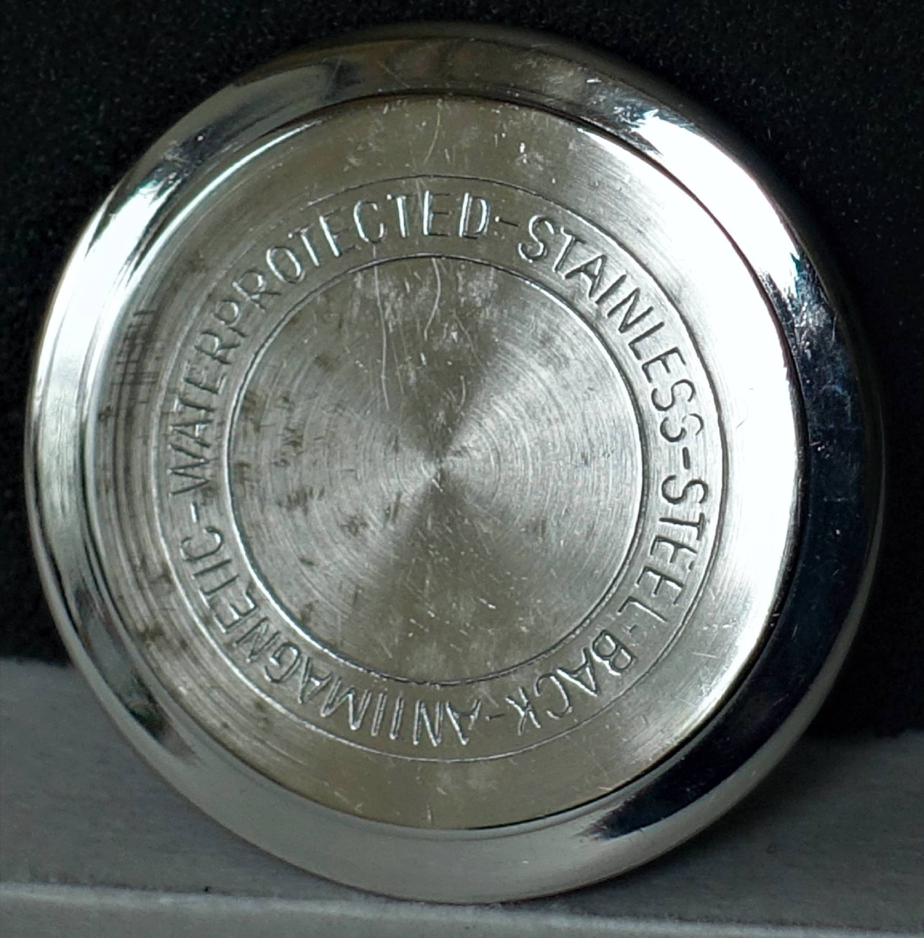 Runder silberfarbener Uhrenboden aus Metall mit Gravur.