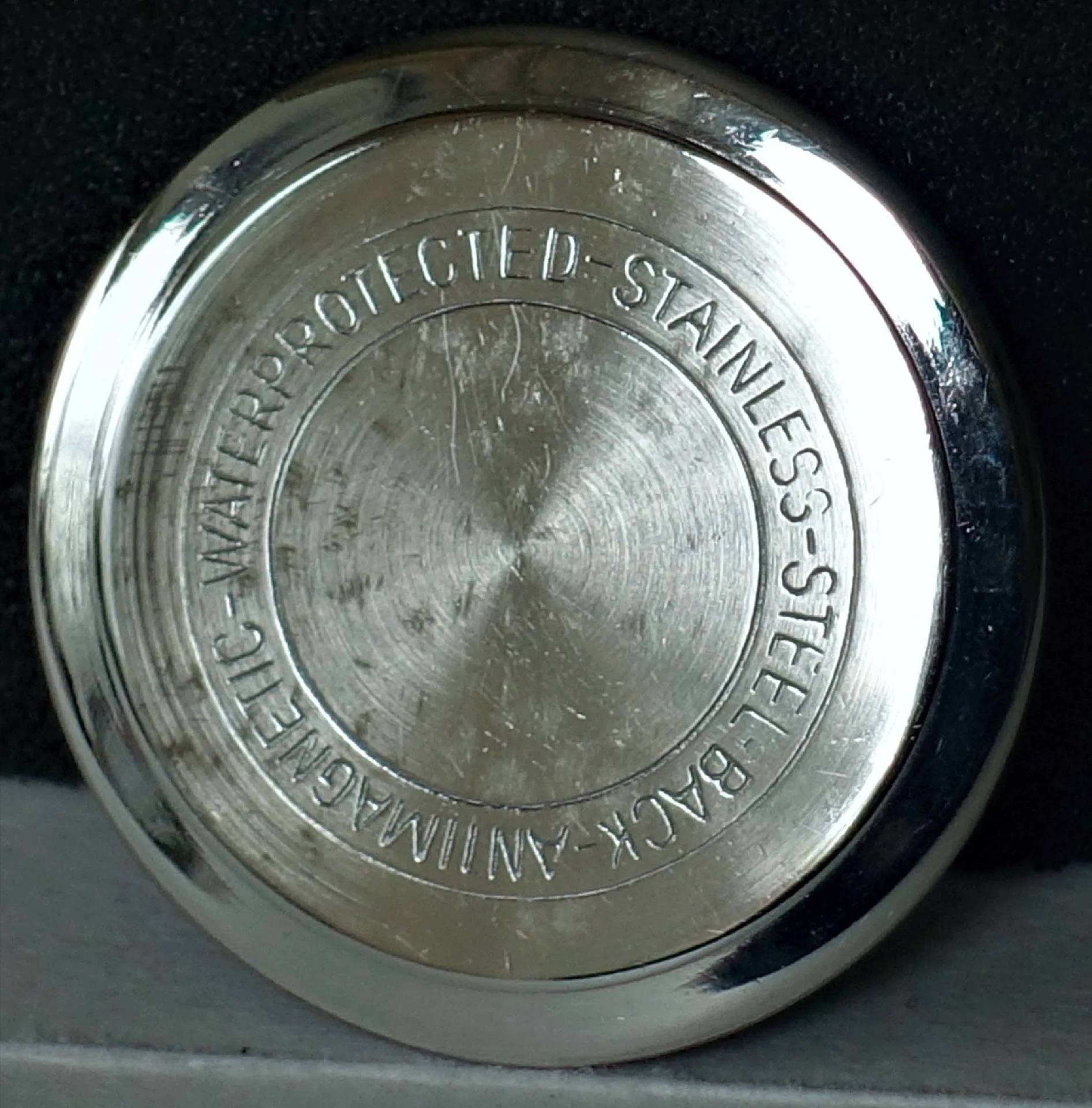 Runder silberfarbener Uhrenboden aus Metall mit Gravur.