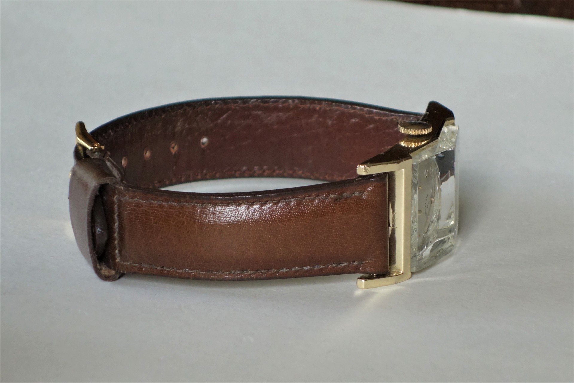 Armbanduhr mit braunem Lederarmband und eckigem Gehäuse in heller Farbe.