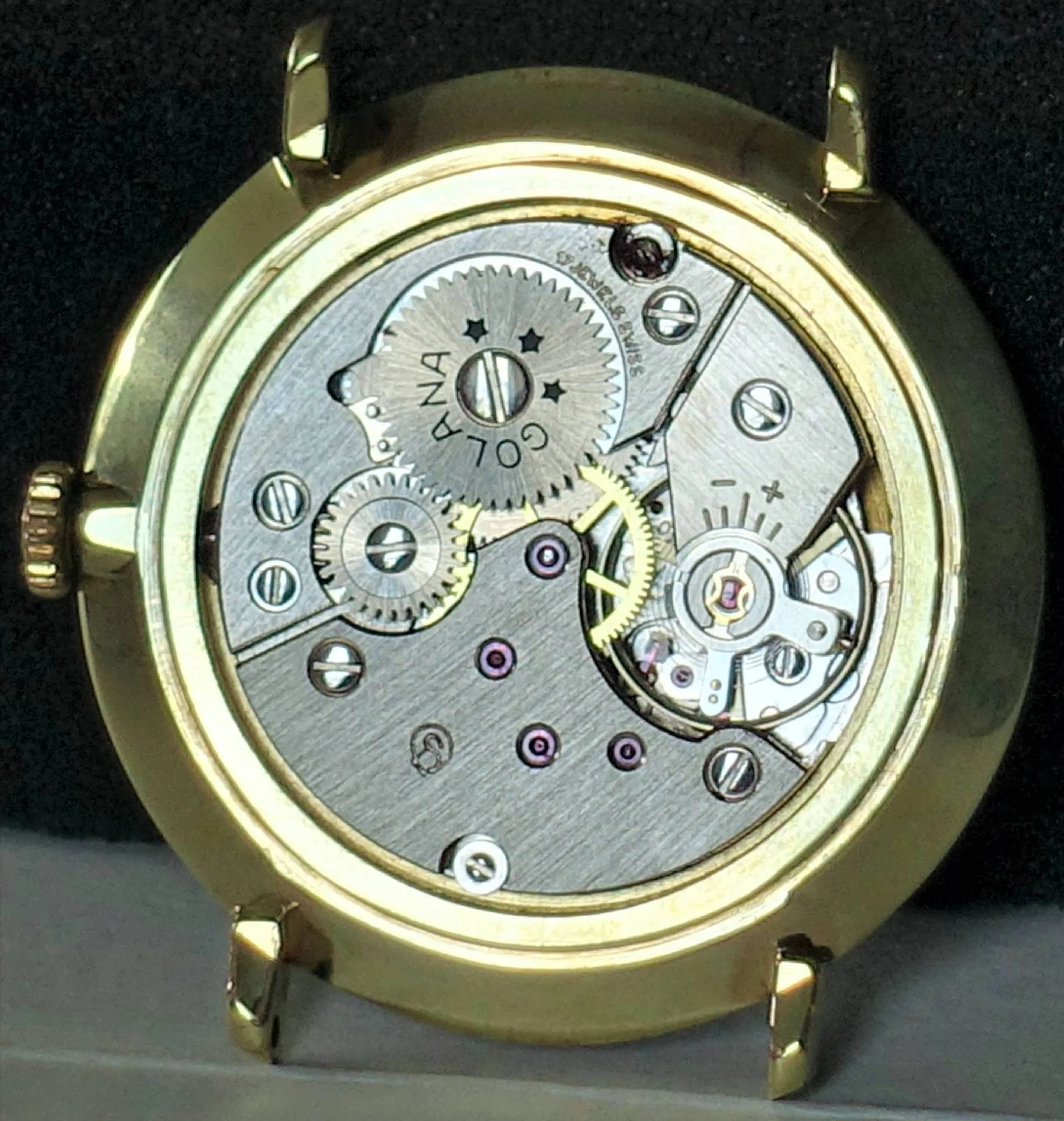Mechanisches Uhrwerk in einem goldfarbenen Gehäuse mit sichtbaren Zahnrädern und Schrauben.