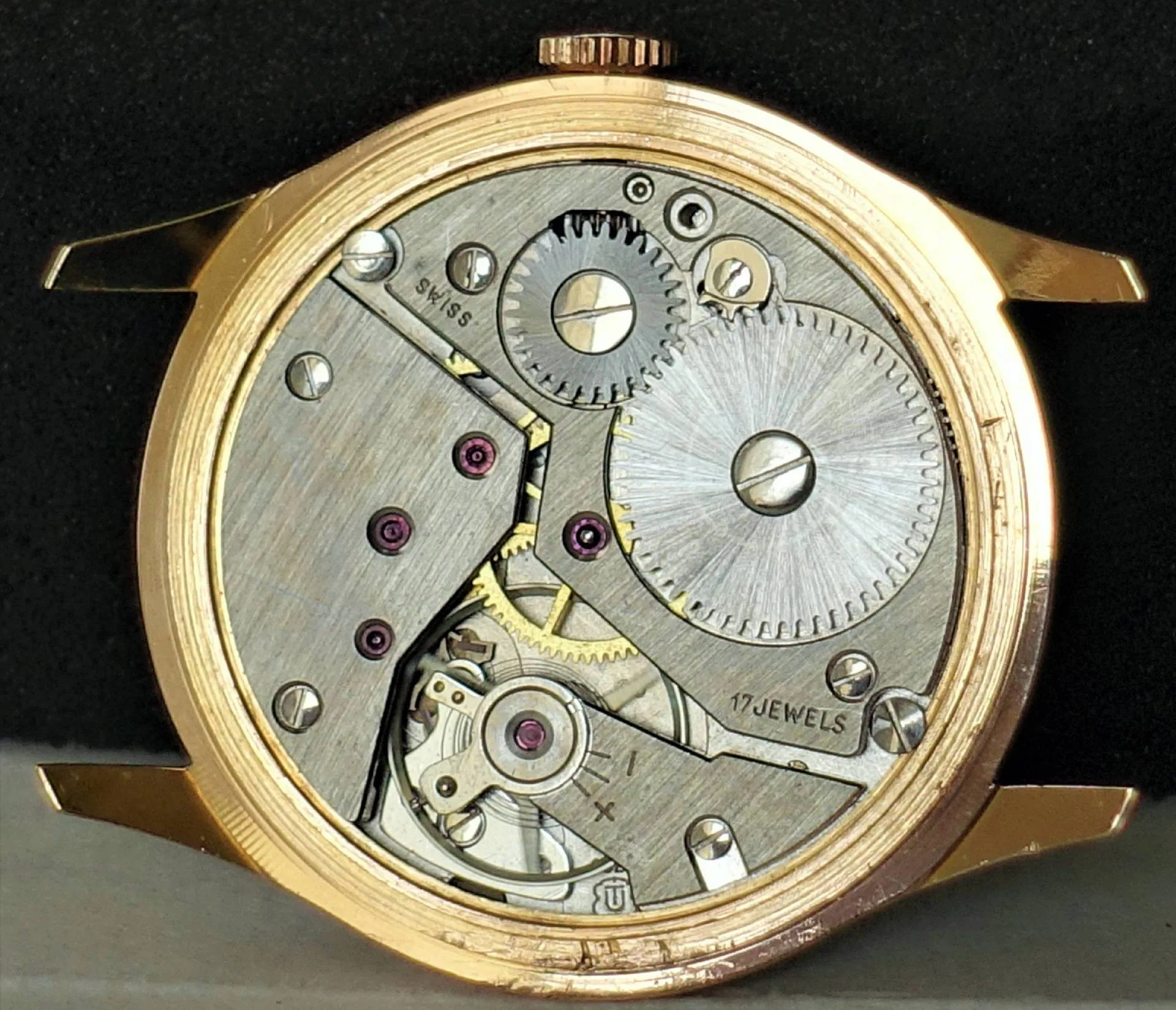 Silbernes Uhrwerk im goldfarbenen Gehäuse Das Bild zeigt das geöffnete Gehäuse einer Armbanduhr mit einem silberfarbenen mechanischen Uhrwerk und goldfarbenem Gehäuserand.