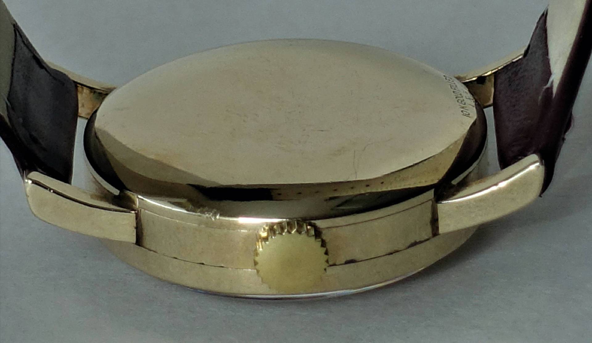 Detailansicht einer klassischen Armbanduhr mit goldenem Gehäuse und braunem Lederarmband