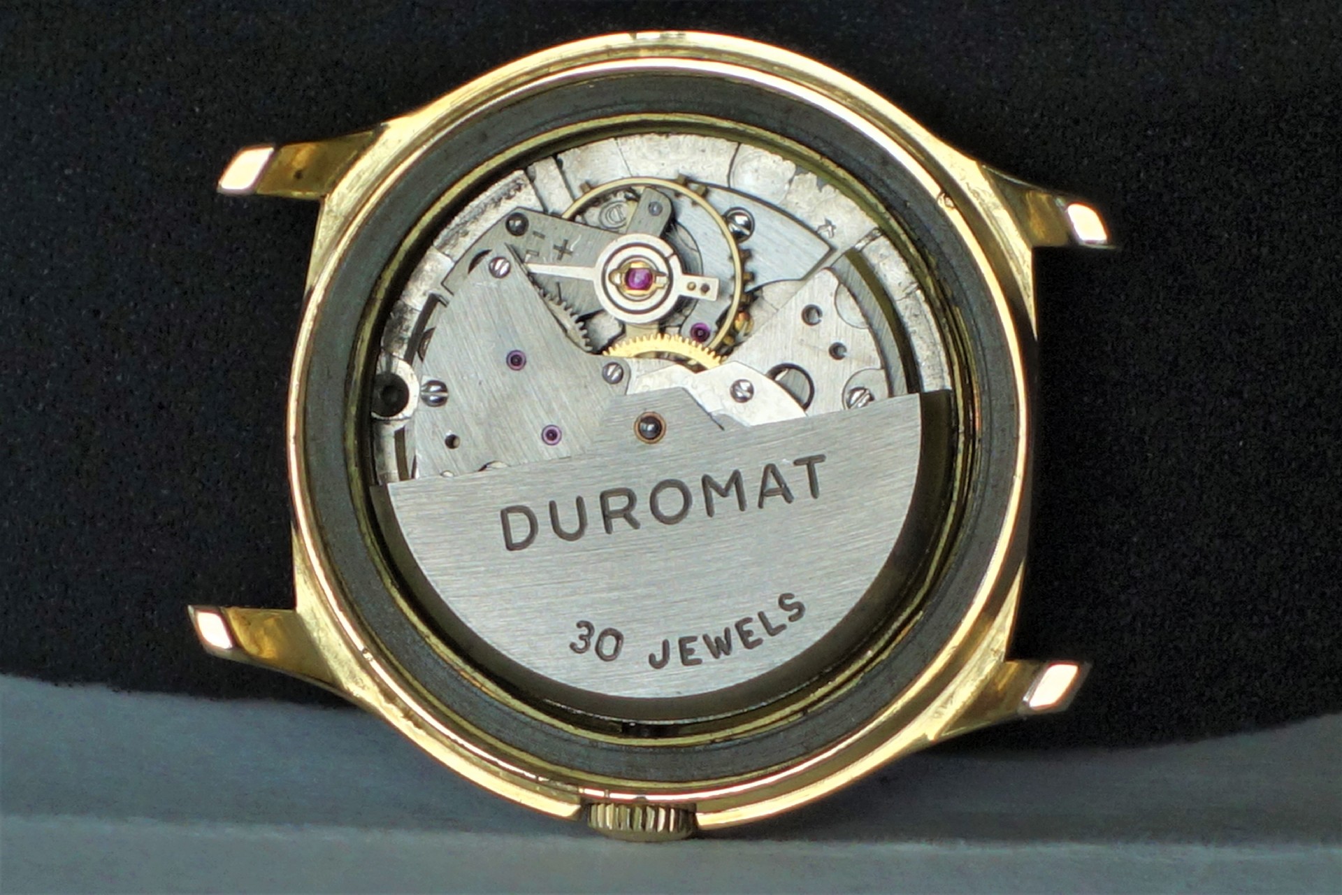 Silberfarbenes Automatik-Uhrwerk mit der Aufschrift "Duromat 30 Jewels" in einem goldfarbenen Gehäuse.