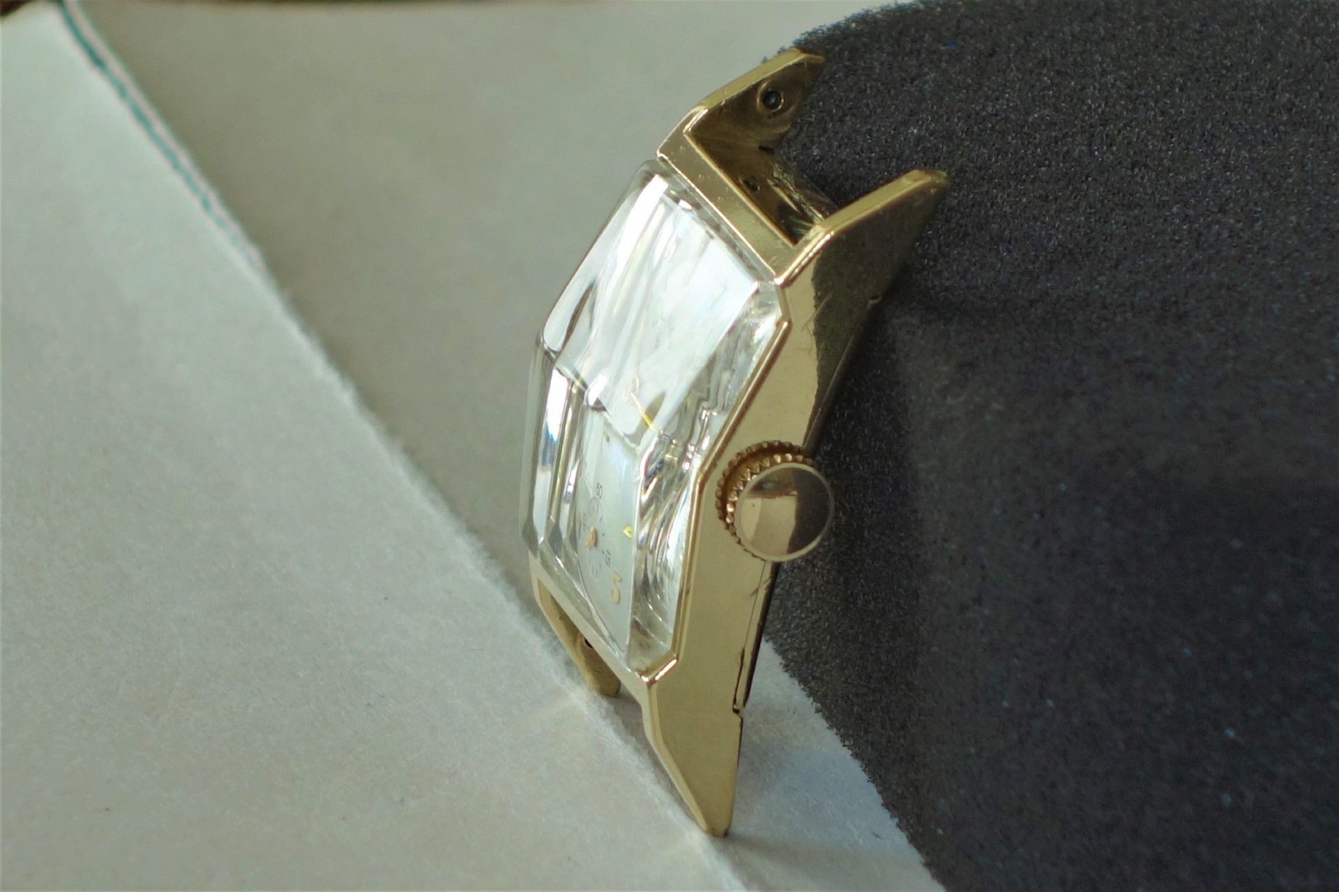 Rechteckiges Uhrgehäuse in goldfarbener Ausführung mit seitlicher Krone und gewölbtem Glas.
