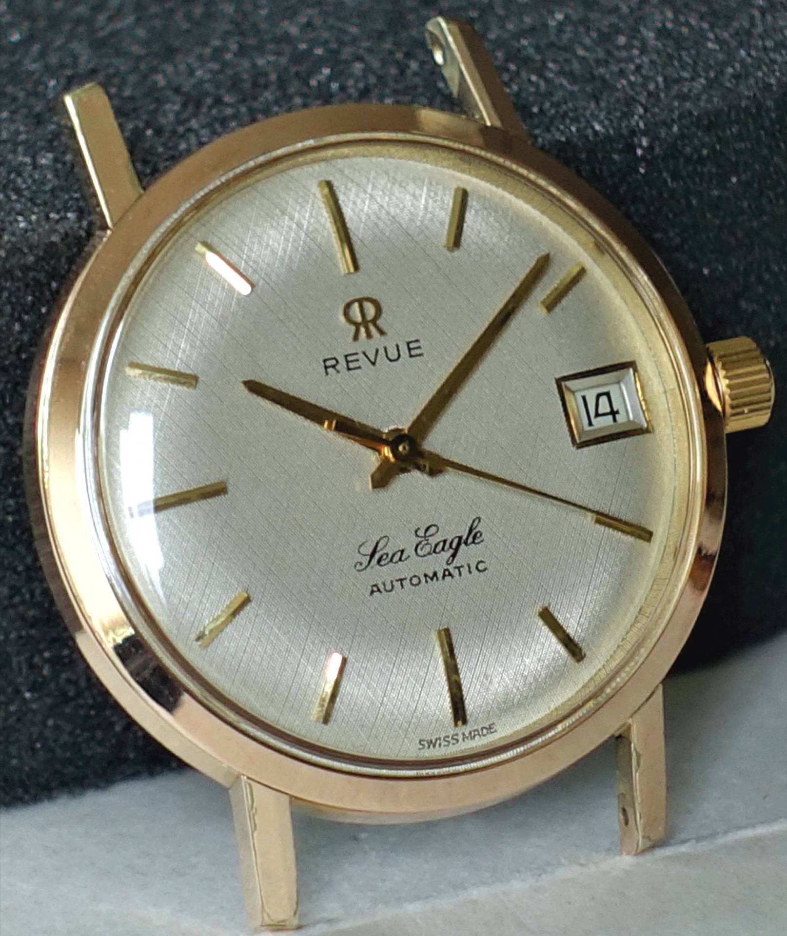 Goldfarbene Armbanduhr mit silberfarbenem Zifferblatt, goldenen Zeigern und Datumsanzeige.