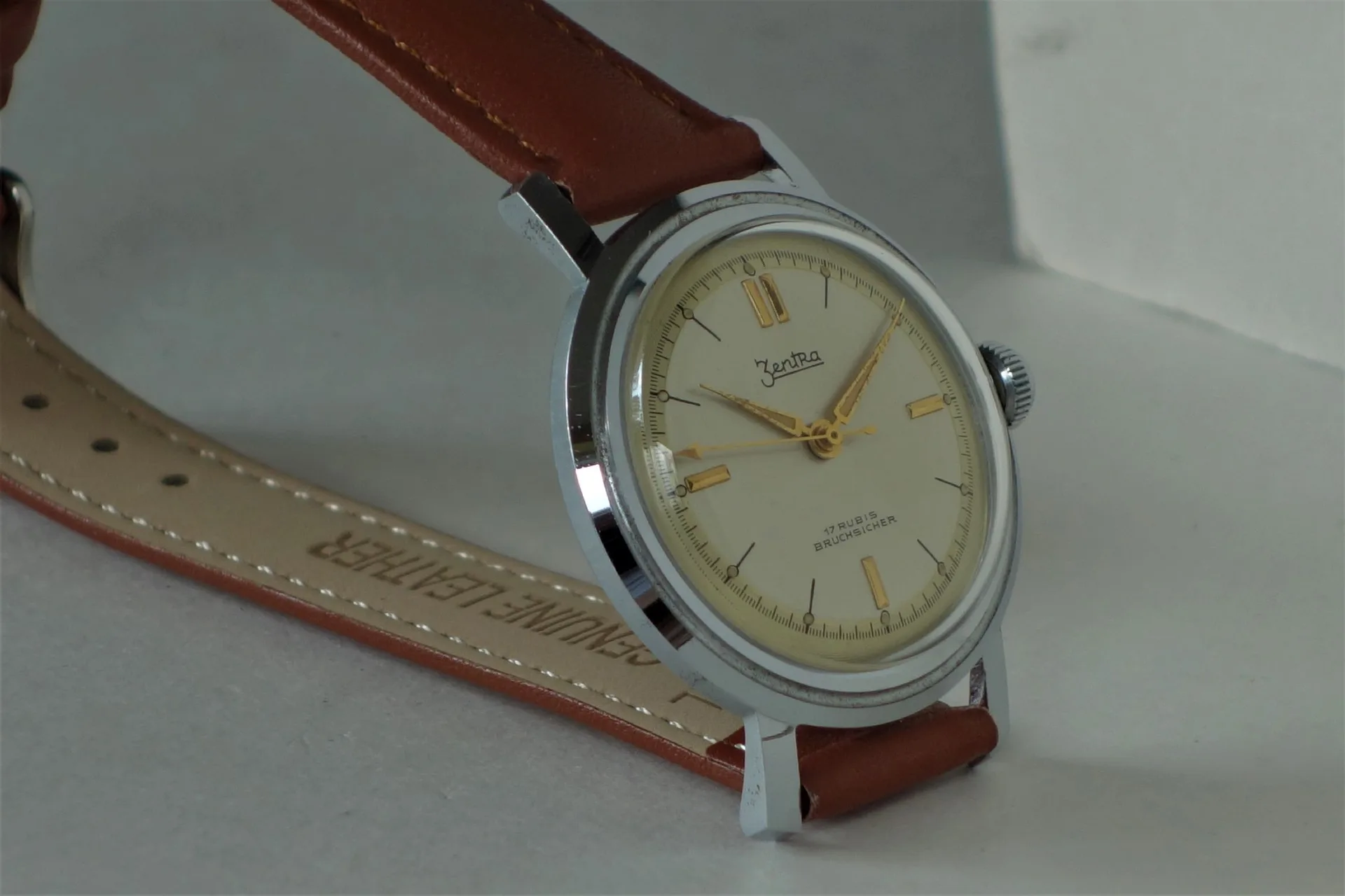 Analoge Armbanduhr mit cremefarbenem Zifferblatt, braunem Lederarmband und silberfarbenem Gehäuse.