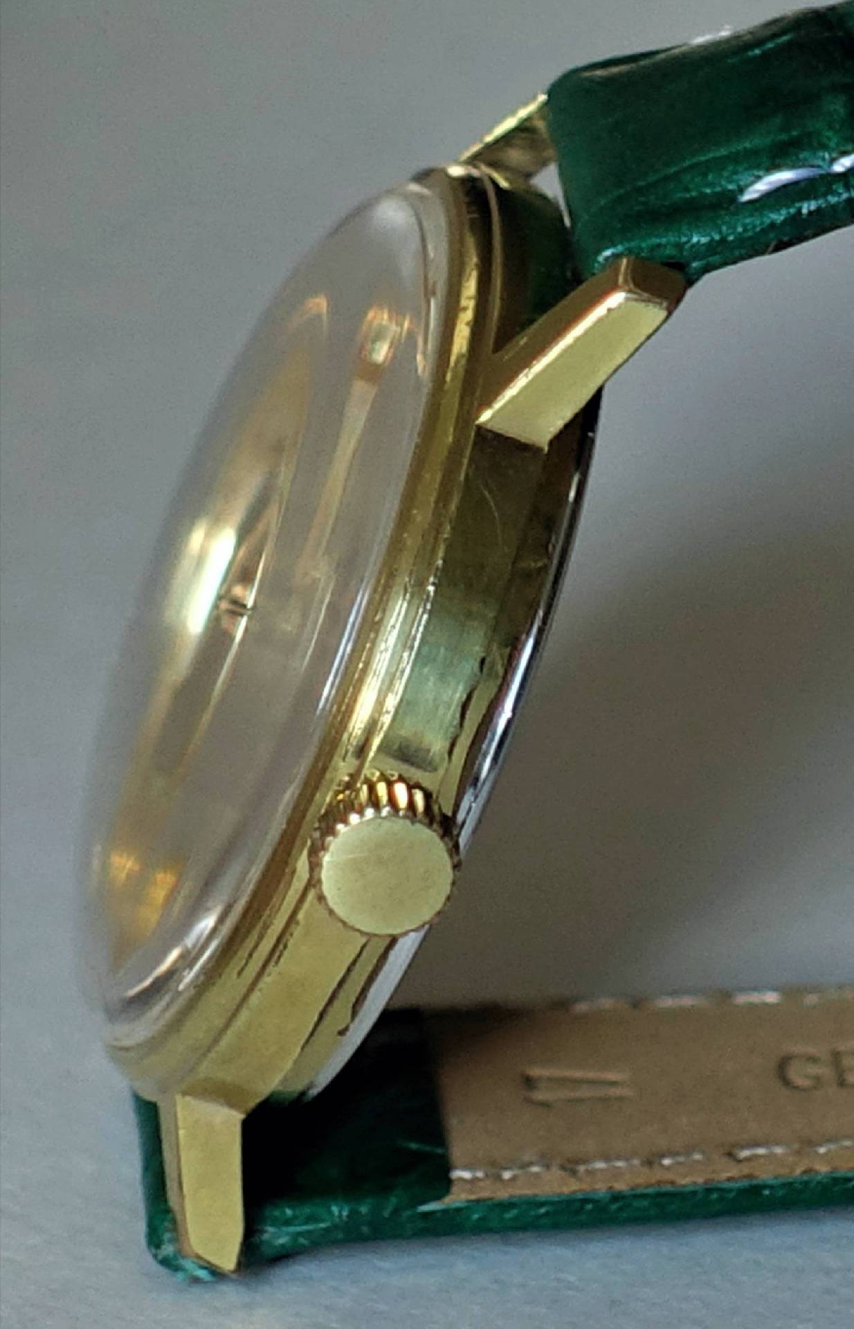Goldfarbene Armbanduhr mit grünem Armband und seitlicher Krone.