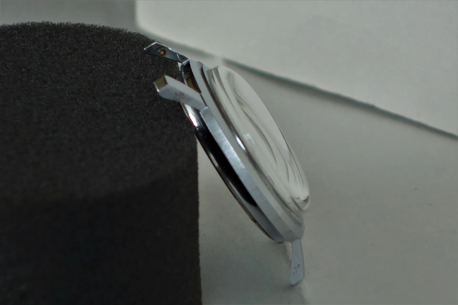 Silberfarbenes Uhrgehäuse mit montiertem Glas, seitliche Ansicht.