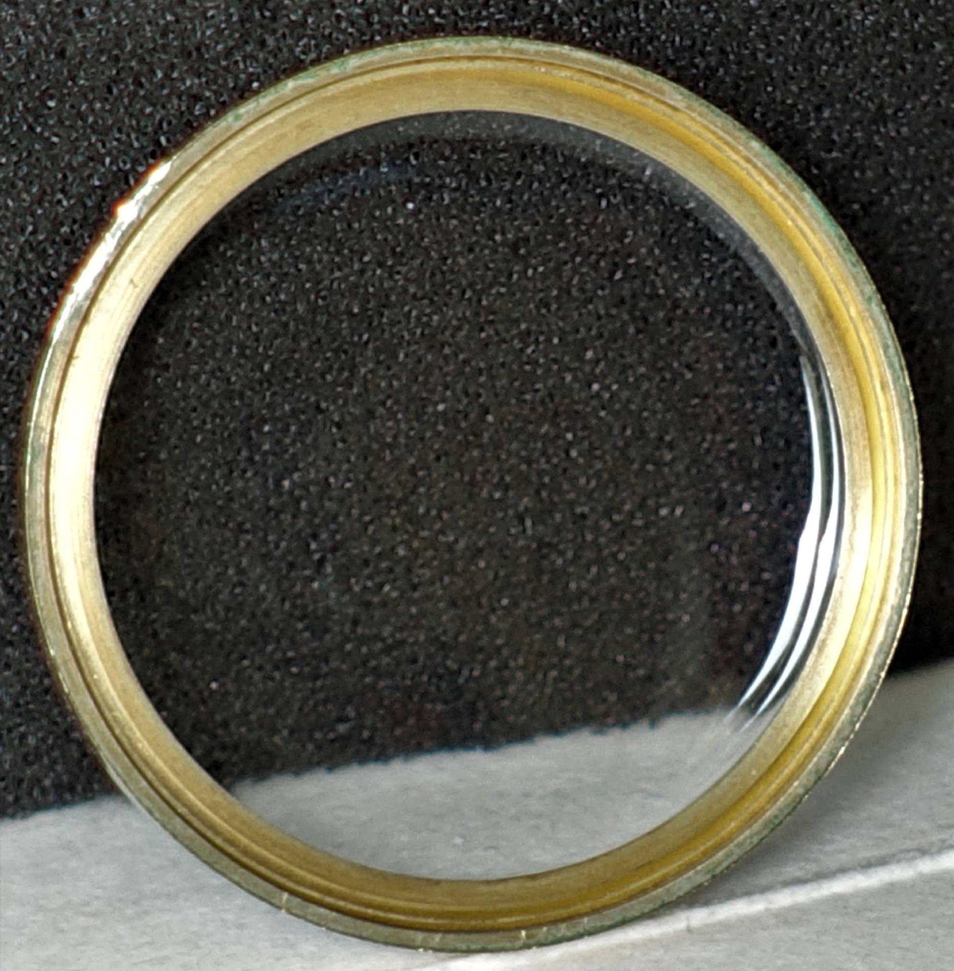Runder Glasrahmen mit goldenem Rand vor schwarzem Hintergrund
