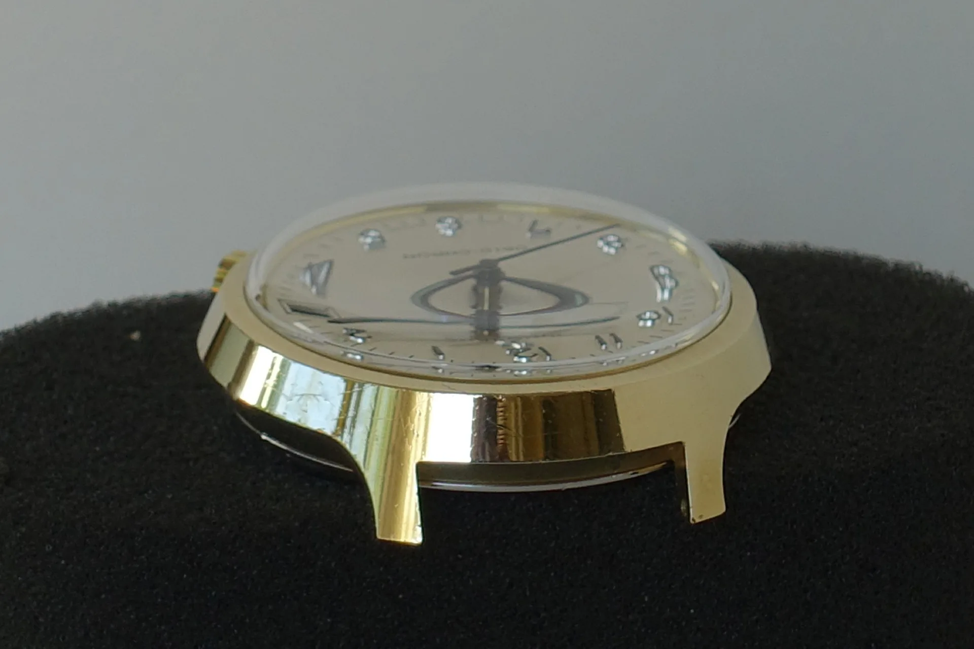 Goldfarbenes Uhrgehäuse mit Zifferblatt und Zeigern, ohne Armband.
