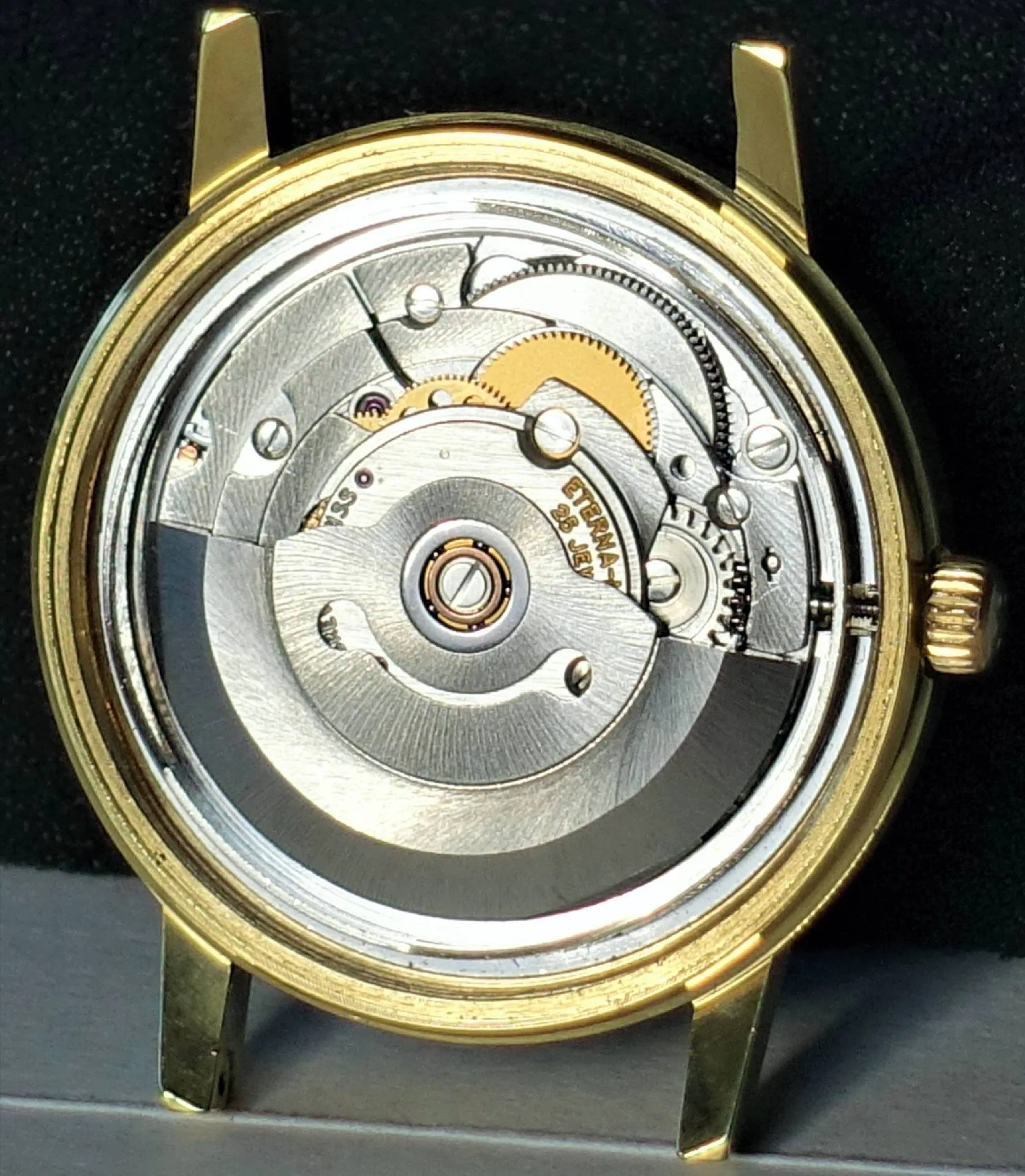 Silberfarbenes Automatik-Uhrwerk in einem goldfarbenen Uhrengehäuse, Rückansicht.