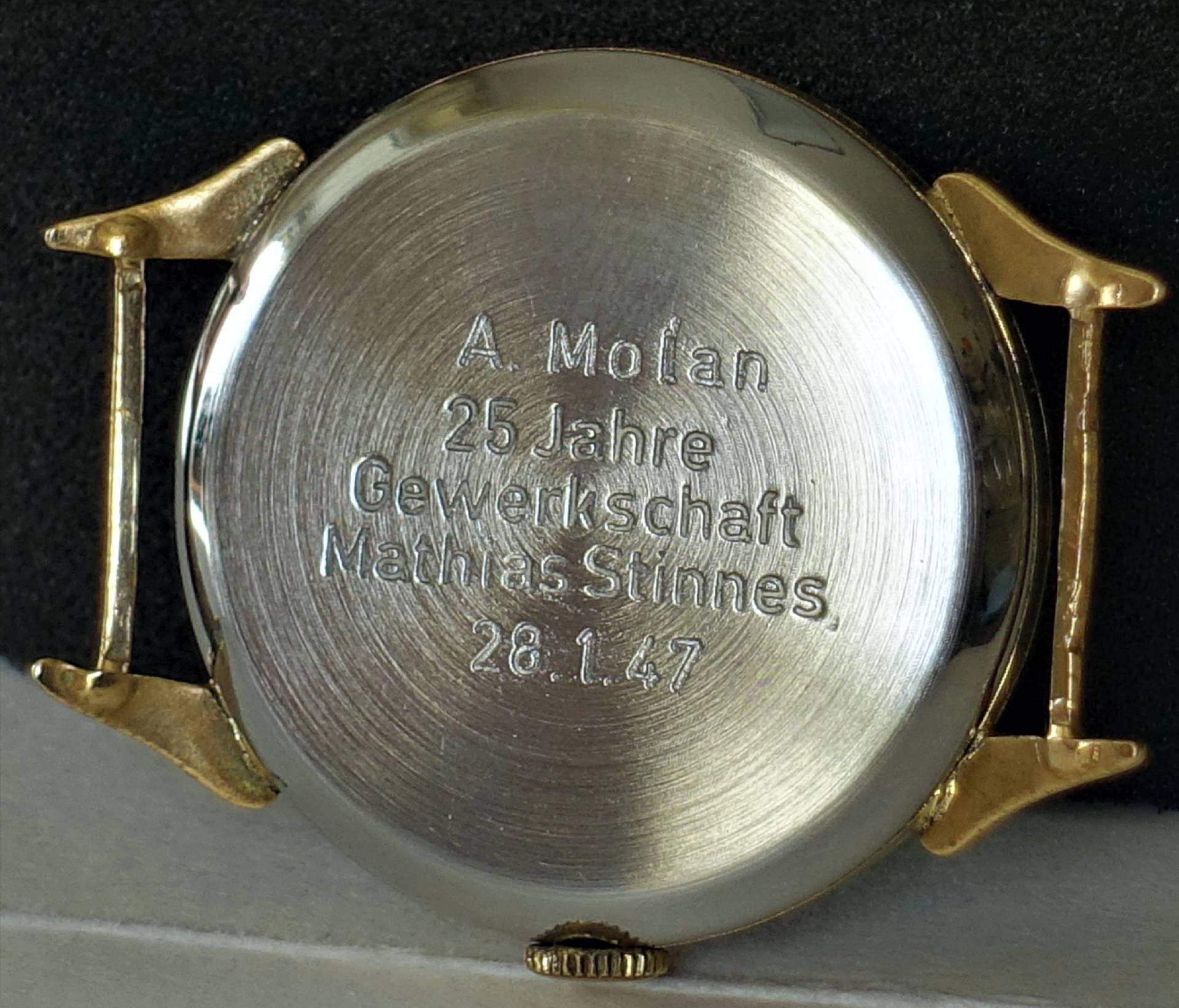 Silberfarbener Uhrboden mit Gravur und goldfarbenen Bandanstößen.