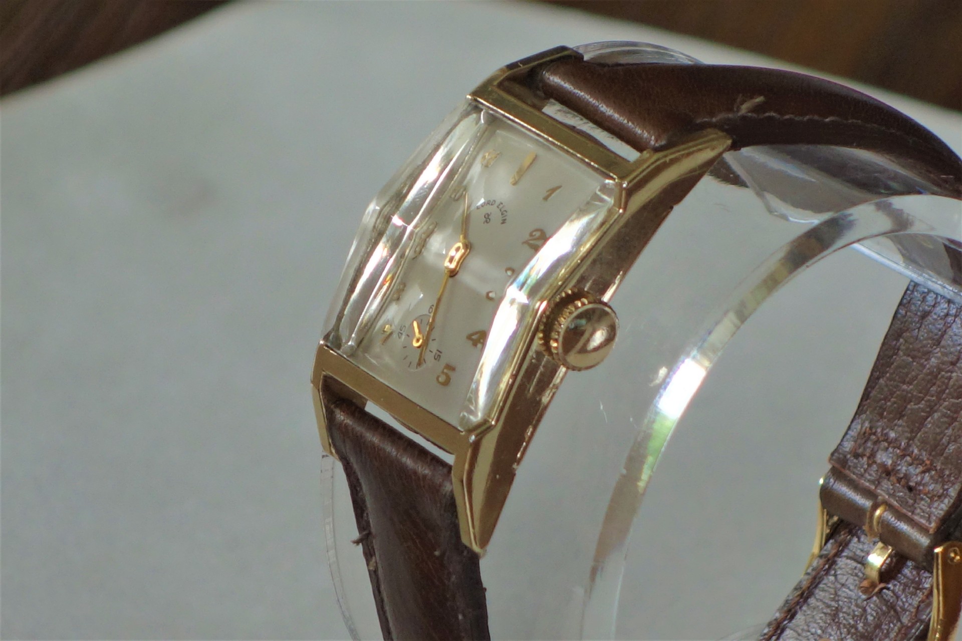 Rechteckige Armbanduhr mit braunem Armband und hellem Zifferblatt.