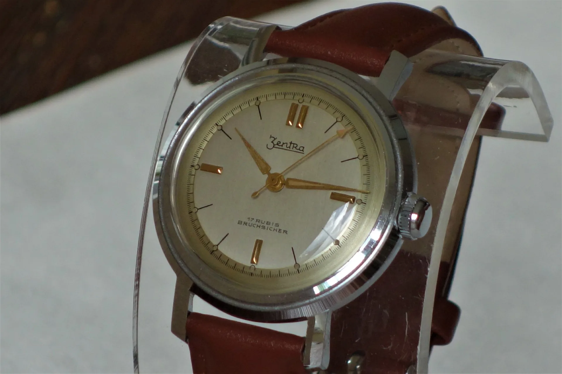 Mechanische Armbanduhr mit beigem Zifferblatt, goldfarbenen Zeigern und braunem Armband.
