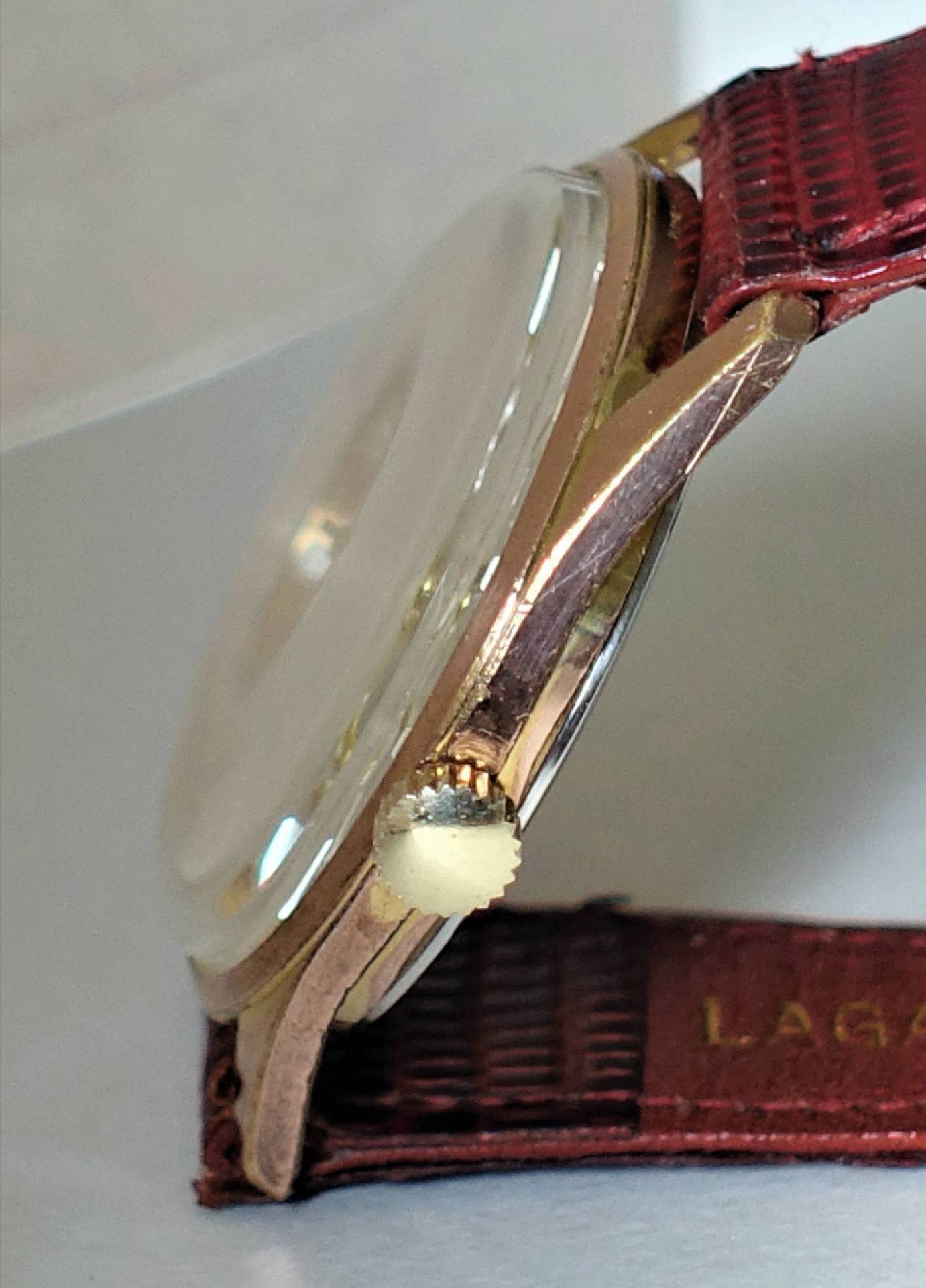 Flache Armbanduhr mit goldfarbenem Gehäuse, rotem Armband und seitlicher Krone.